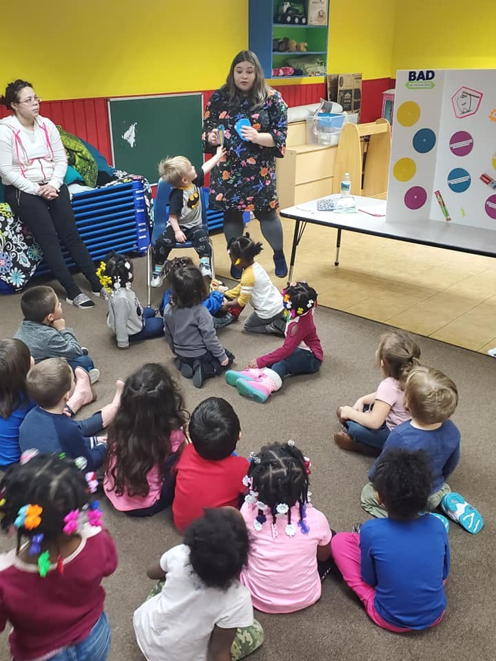 Adult leading a group of children sitting on the floor in a classroom