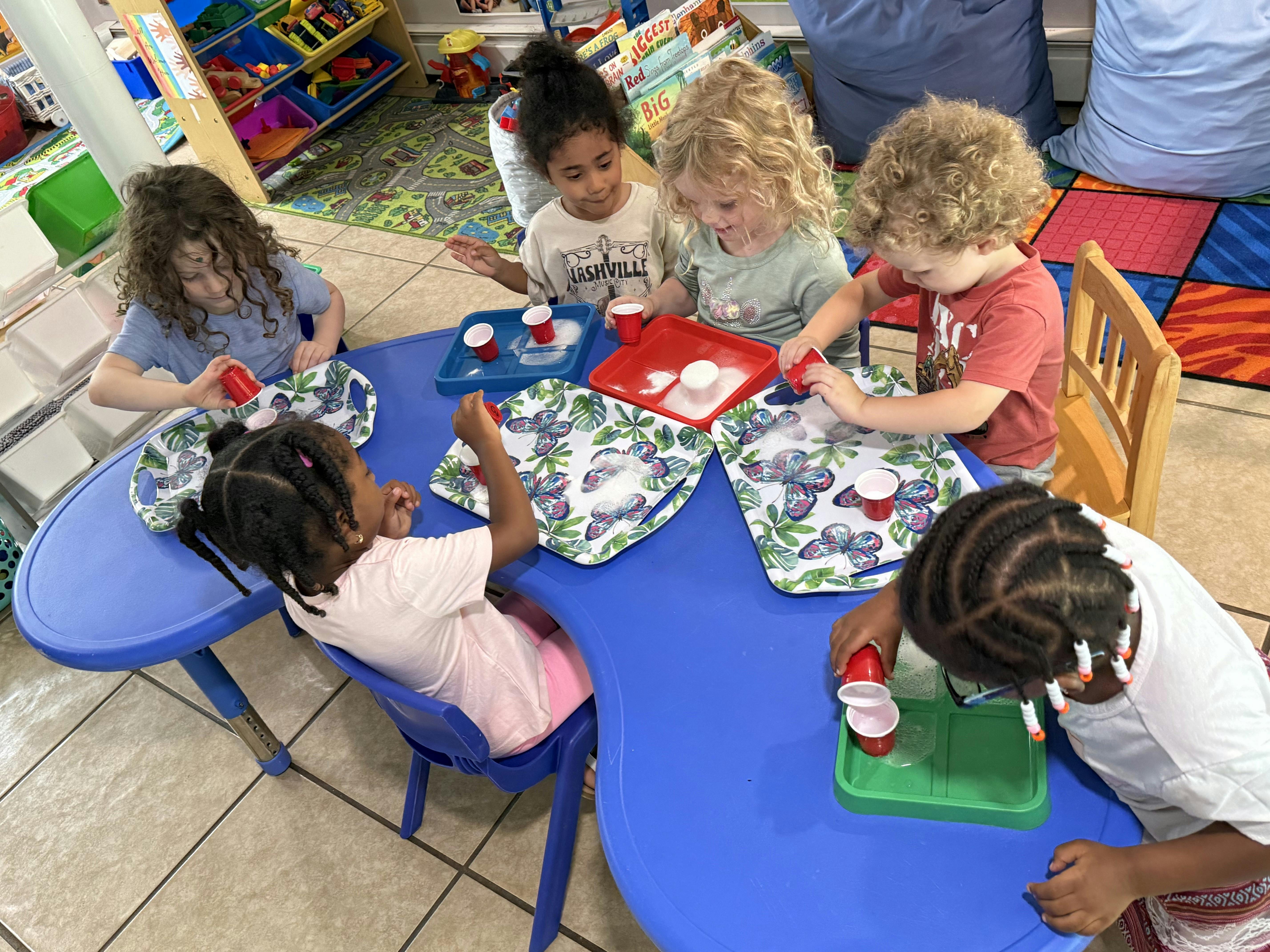 Children at a blue table playing with small cups and trays