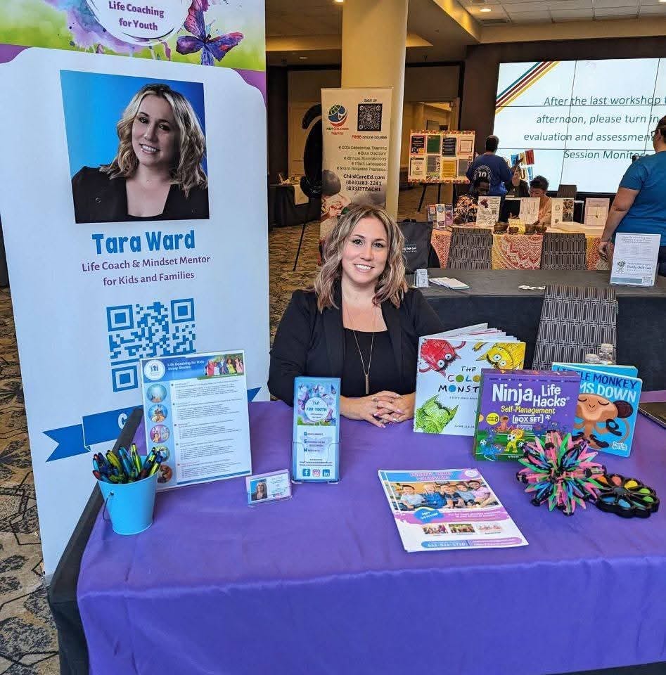 Person sitting at a table with books and a banner with their photo