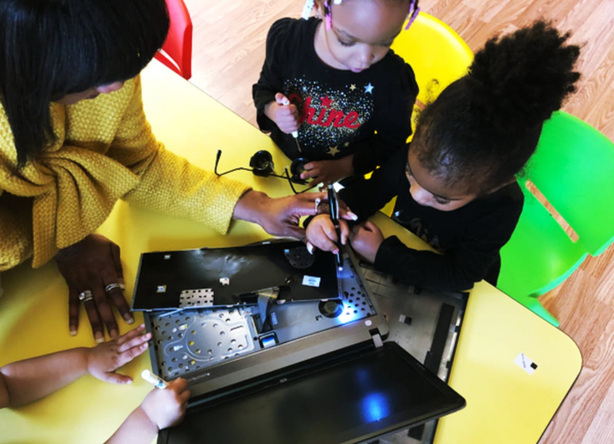 Person and two children working on a disassembled laptop