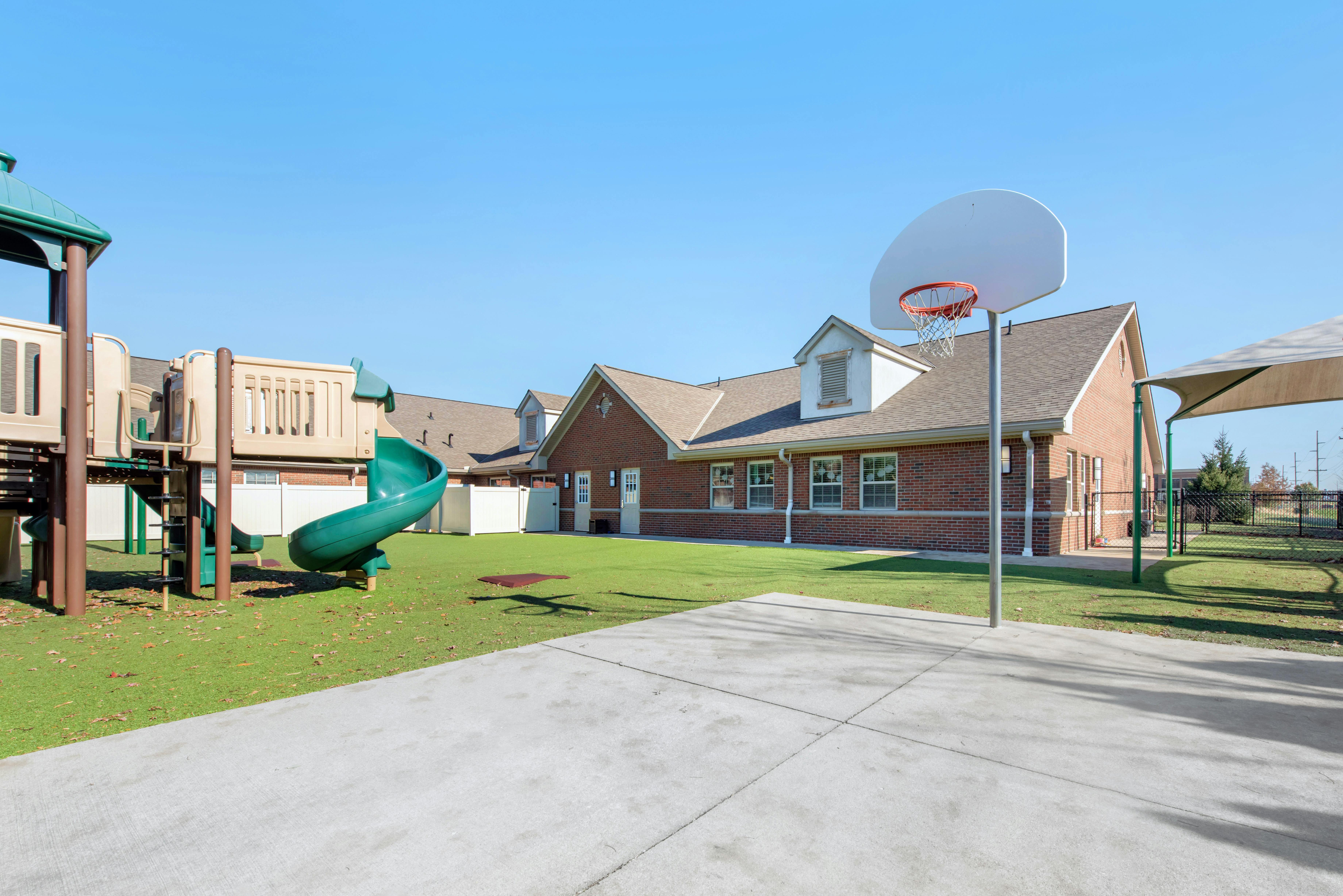 Playground equipment and a basketball hoop next to a brick building