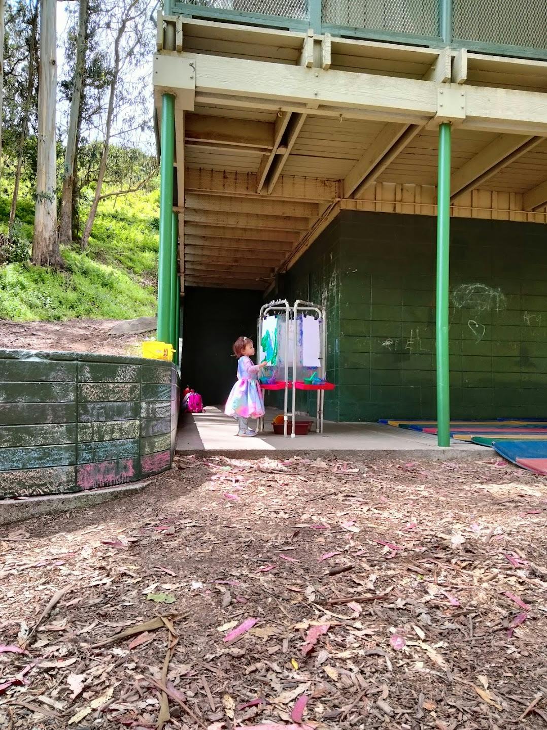 Child standing at an easel under an elevated structure
