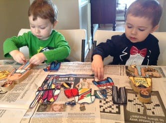 Two children playing with wooden puzzles on a newspaper-covered table