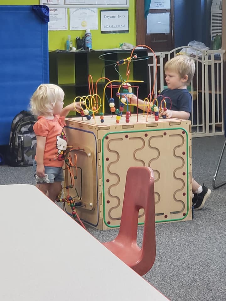 Two children playing with a large wooden activity cube in a classroom