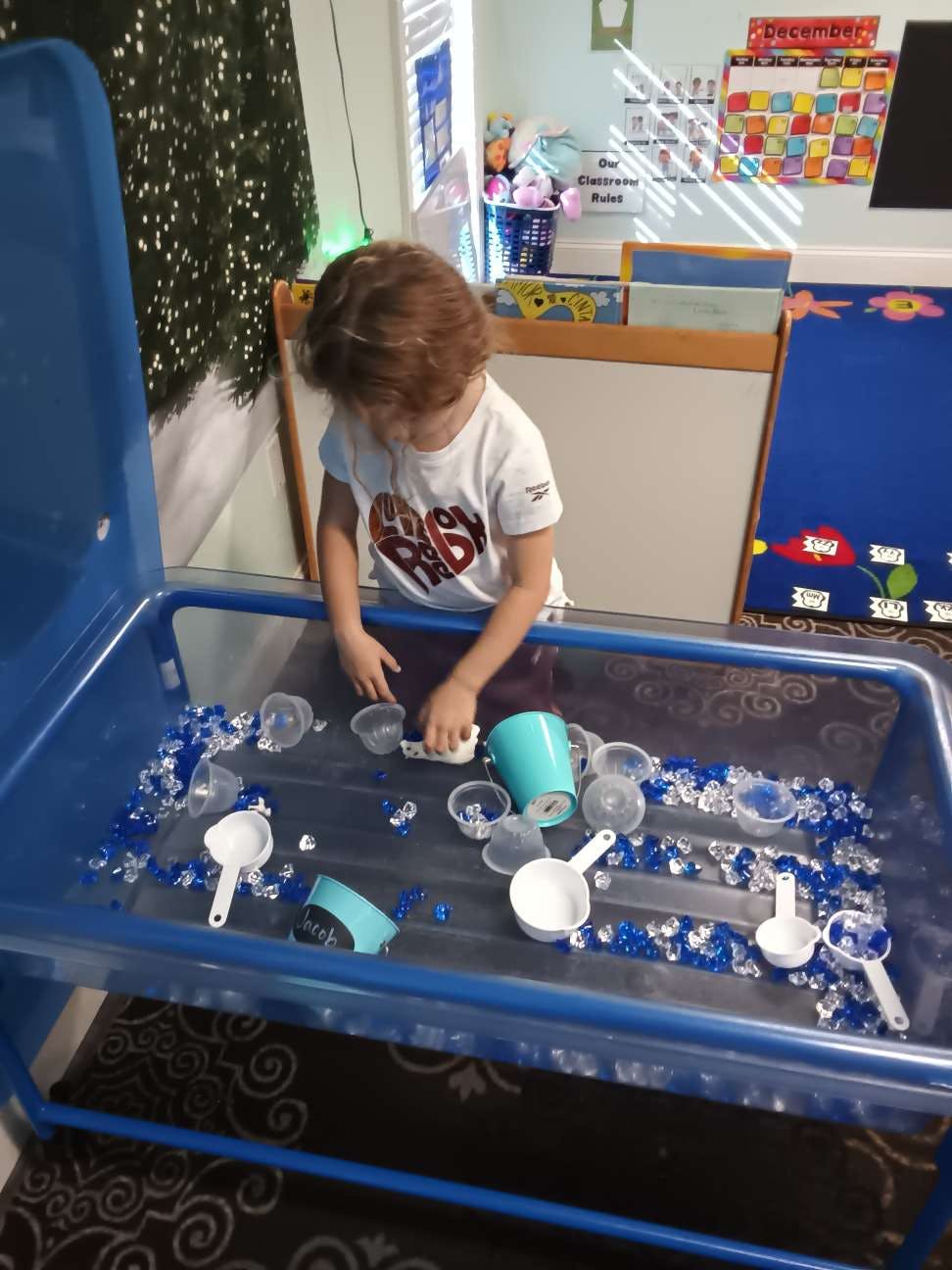 Child playing with scoops and blue objects in a sensory table
