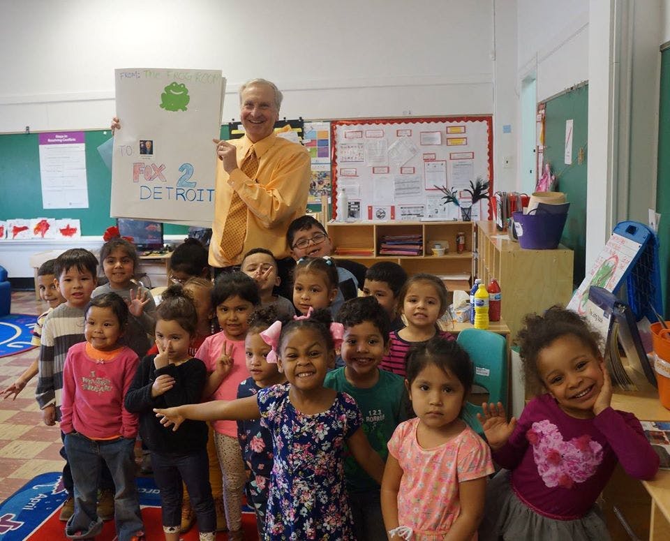 Adult person holding a sign with text "FIX 2 DETROIT" and children in a classroom