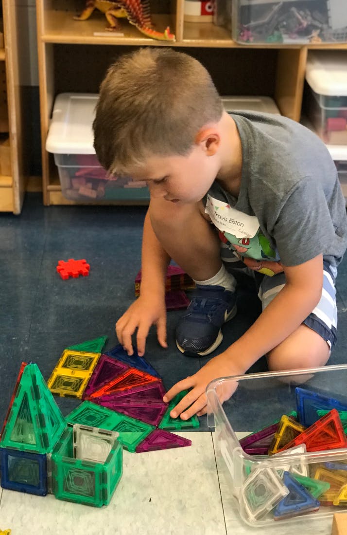 Child playing with colorful magnetic building tiles on the floor