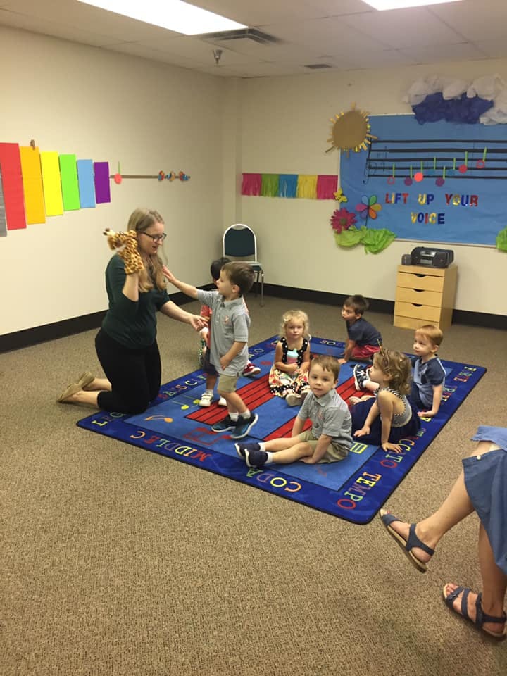 Adult kneeling with children on a rug in a classroom
