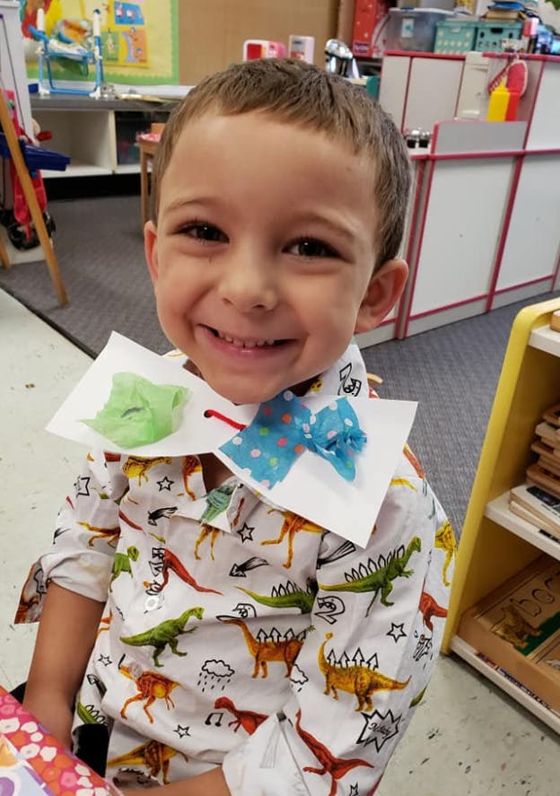 Child wearing a dinosaur print shirt and a paper collar with a blue bow