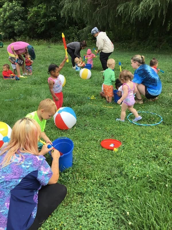 People and children playing with water toys and beach balls in a grassy field