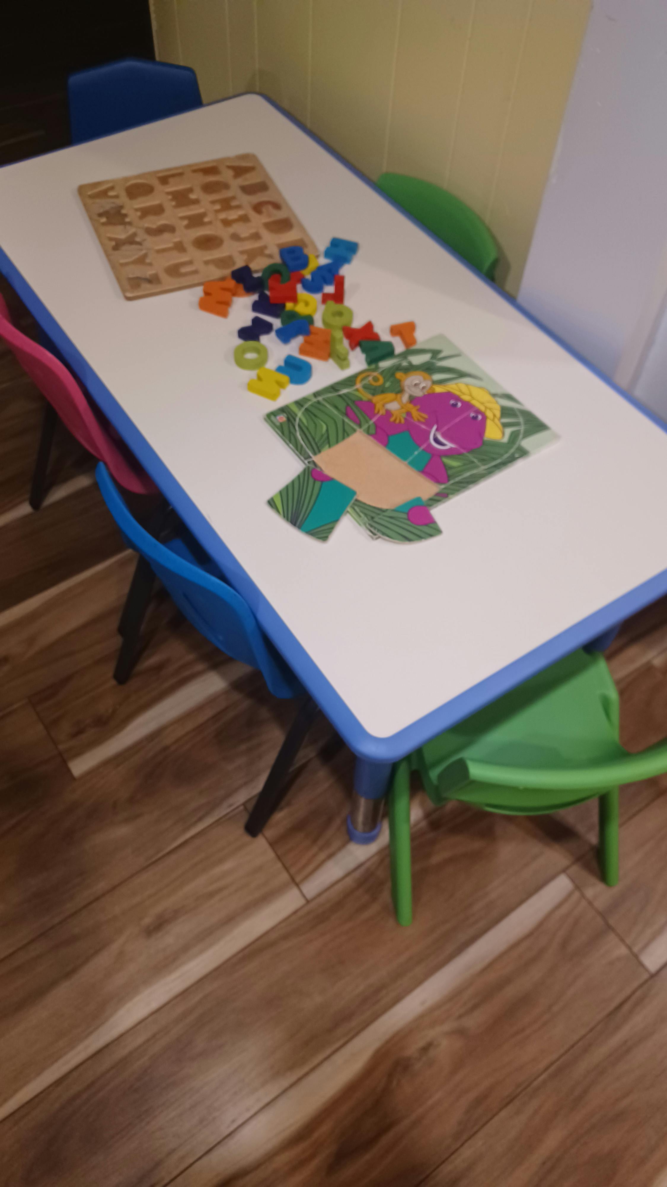 Colorful alphabet puzzle pieces and a dinosaur image on a small activity table