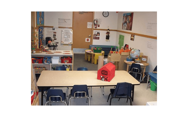 An empty classroom with small tables and chairs, toys, and decorations on the walls