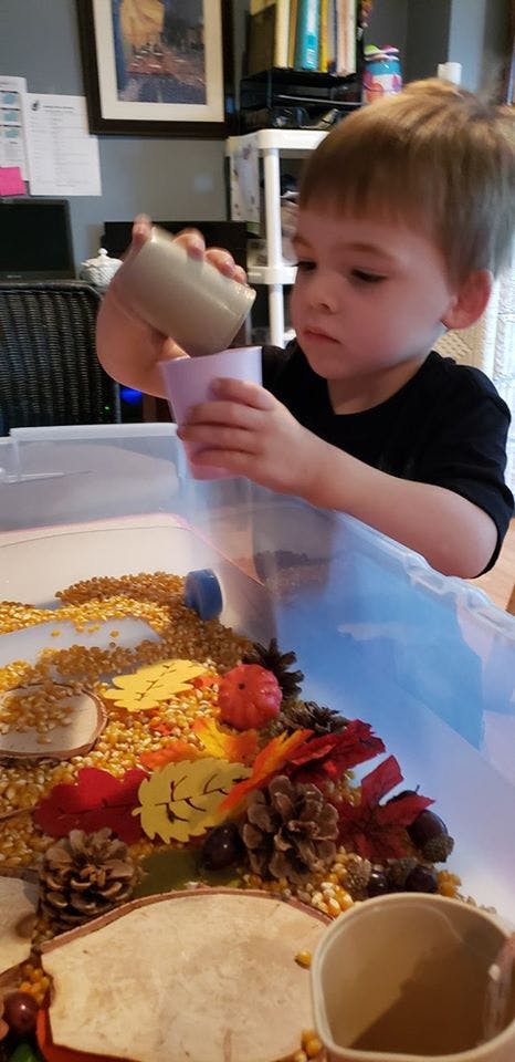 Child pouring from one cup into another over a sensory bin