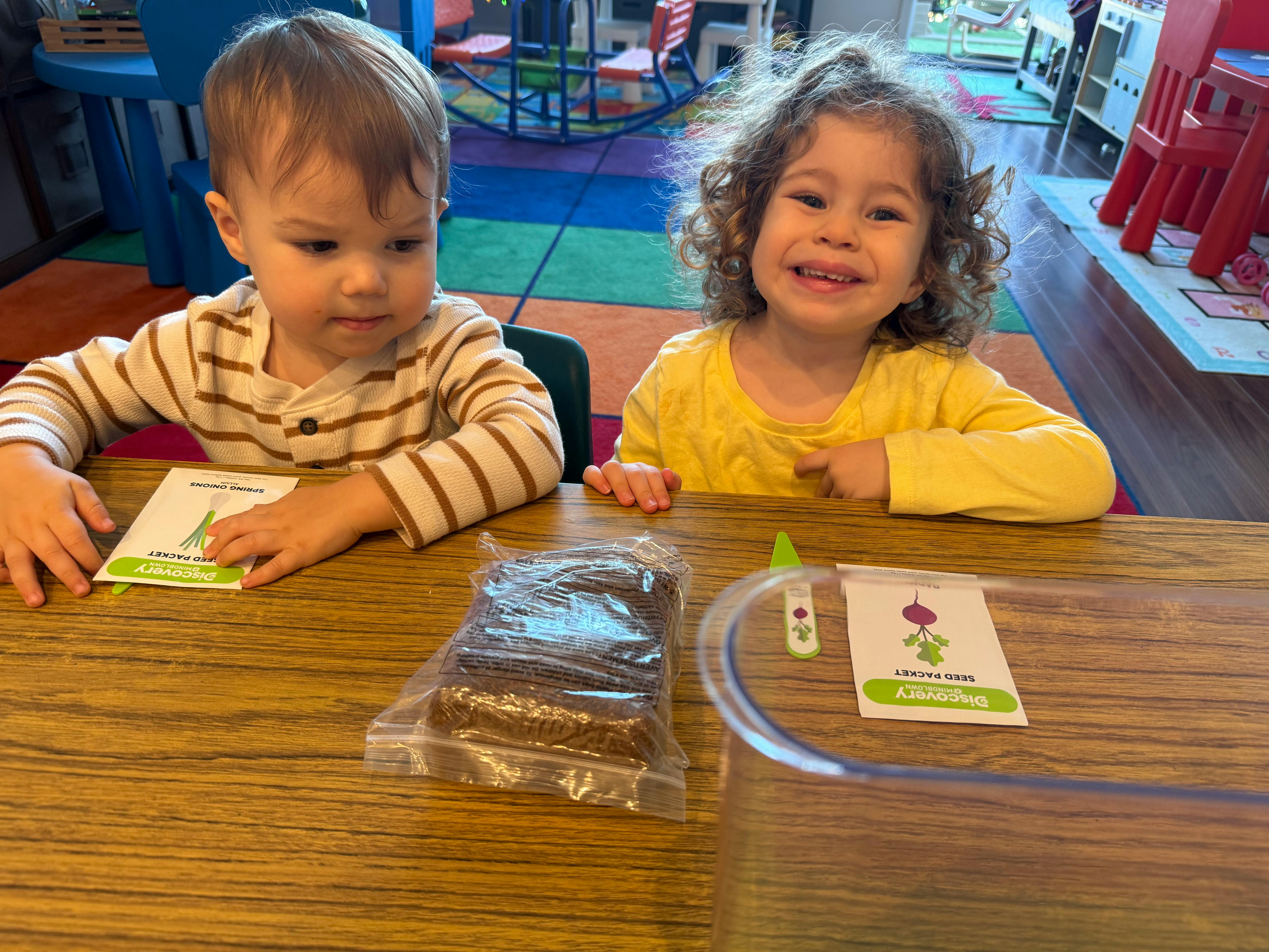 Two children at a table with a seed packet and planting supplies