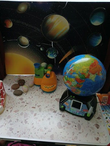 Globe on a stand with toy binoculars and a space-themed background