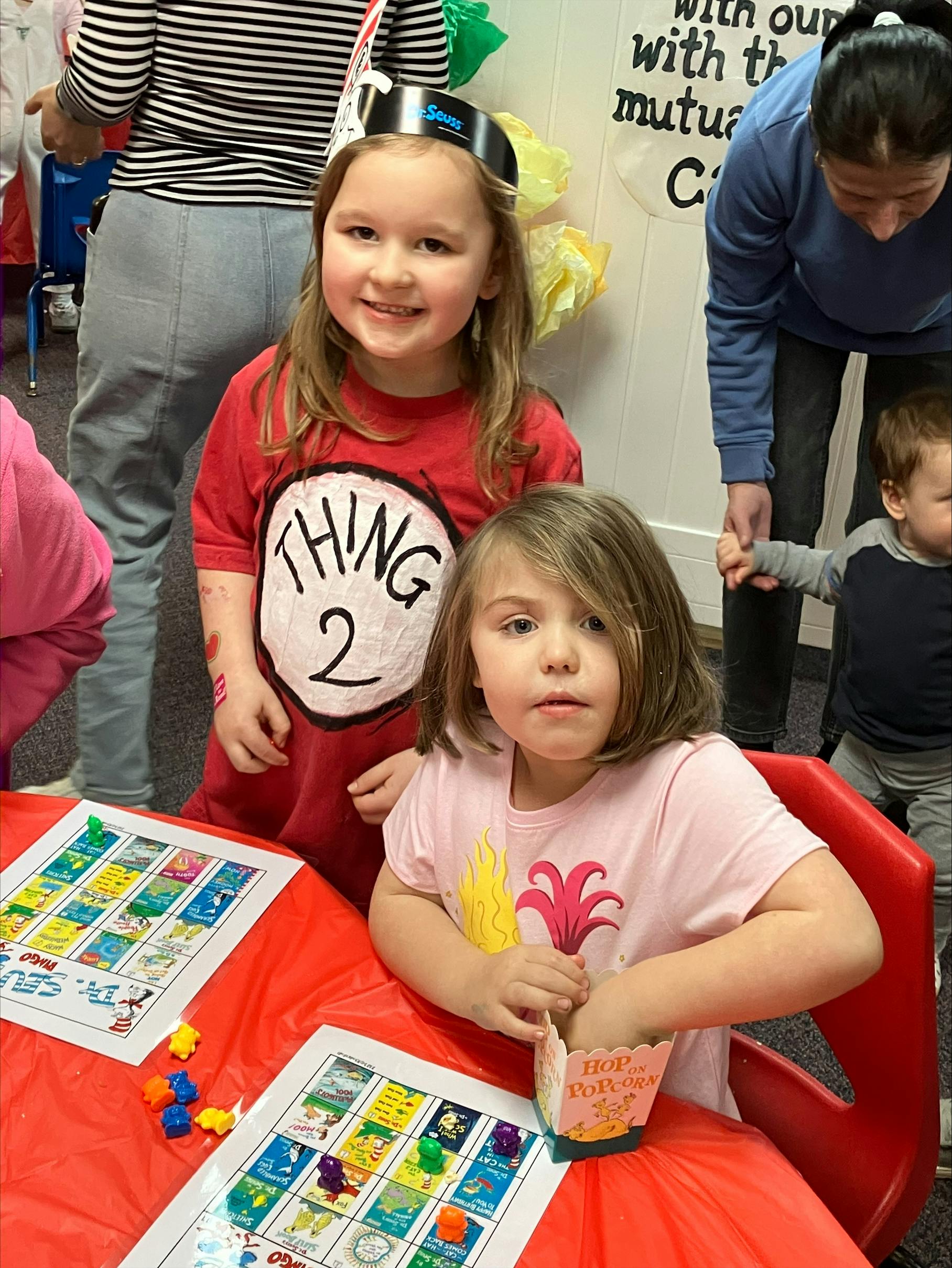 Two children at a table with board games, one wearing a "Thing 2" shirt