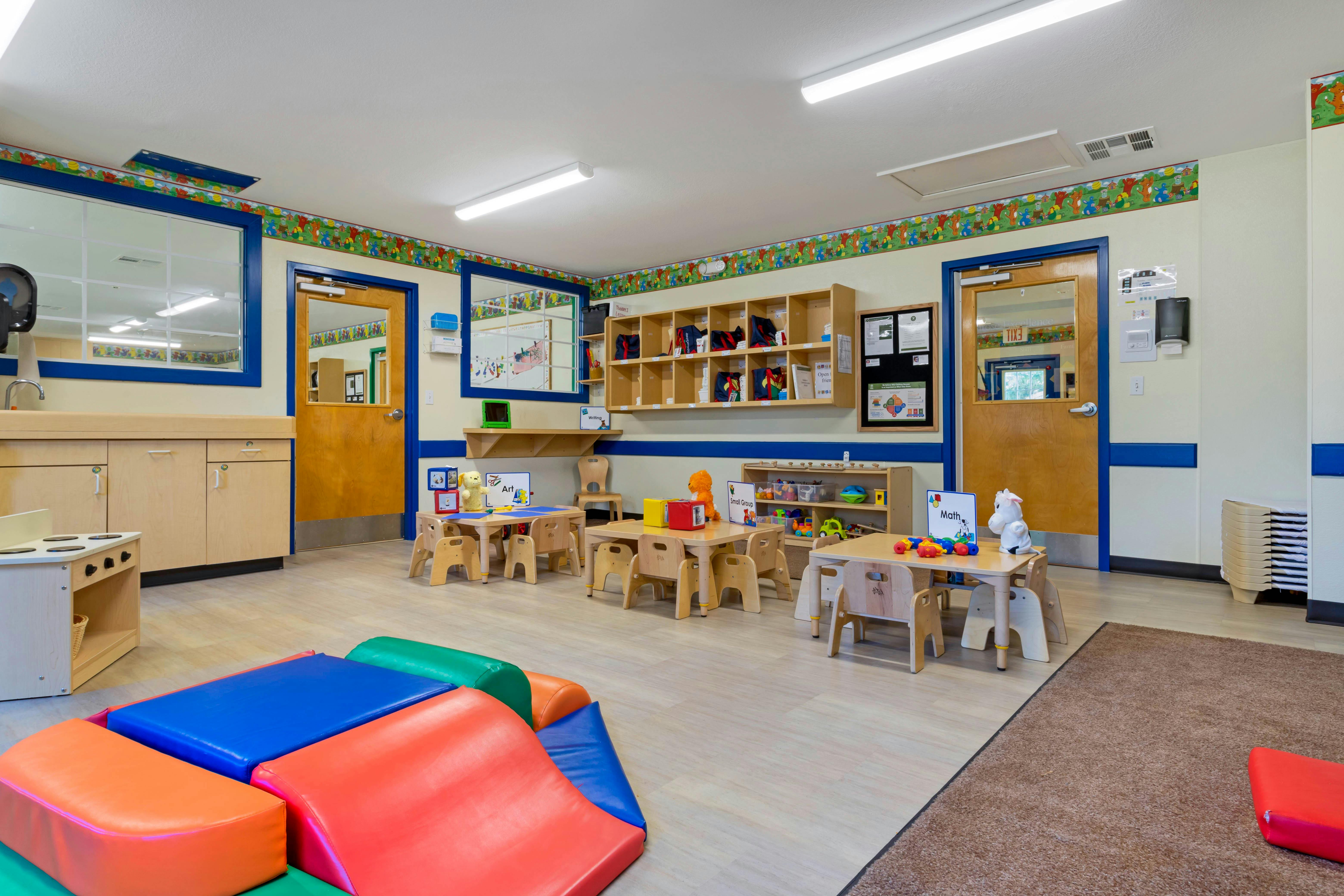 Classroom with small tables and chairs, shelves, play kitchen, and colorful soft play blocks
