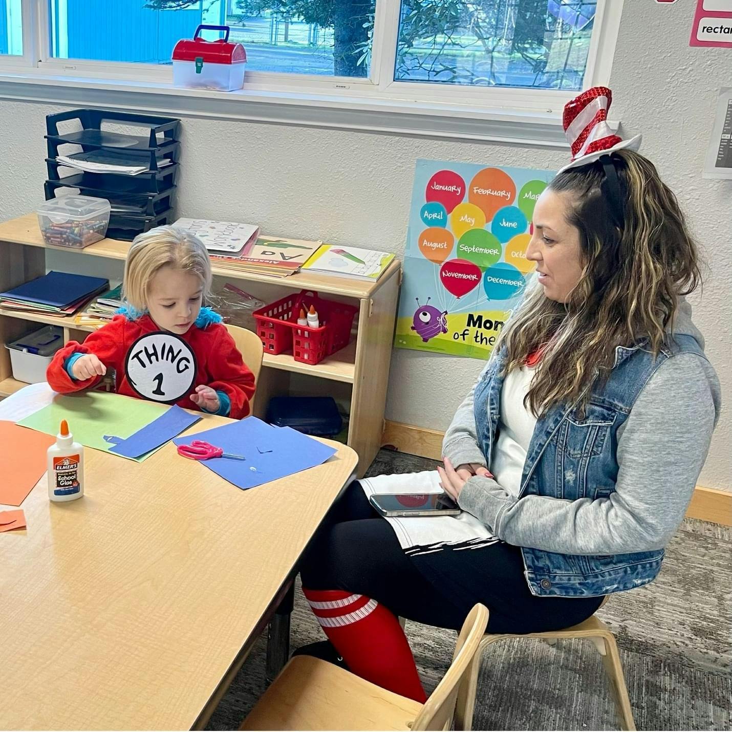 Child in "Thing 1" shirt crafting at a table with an adult