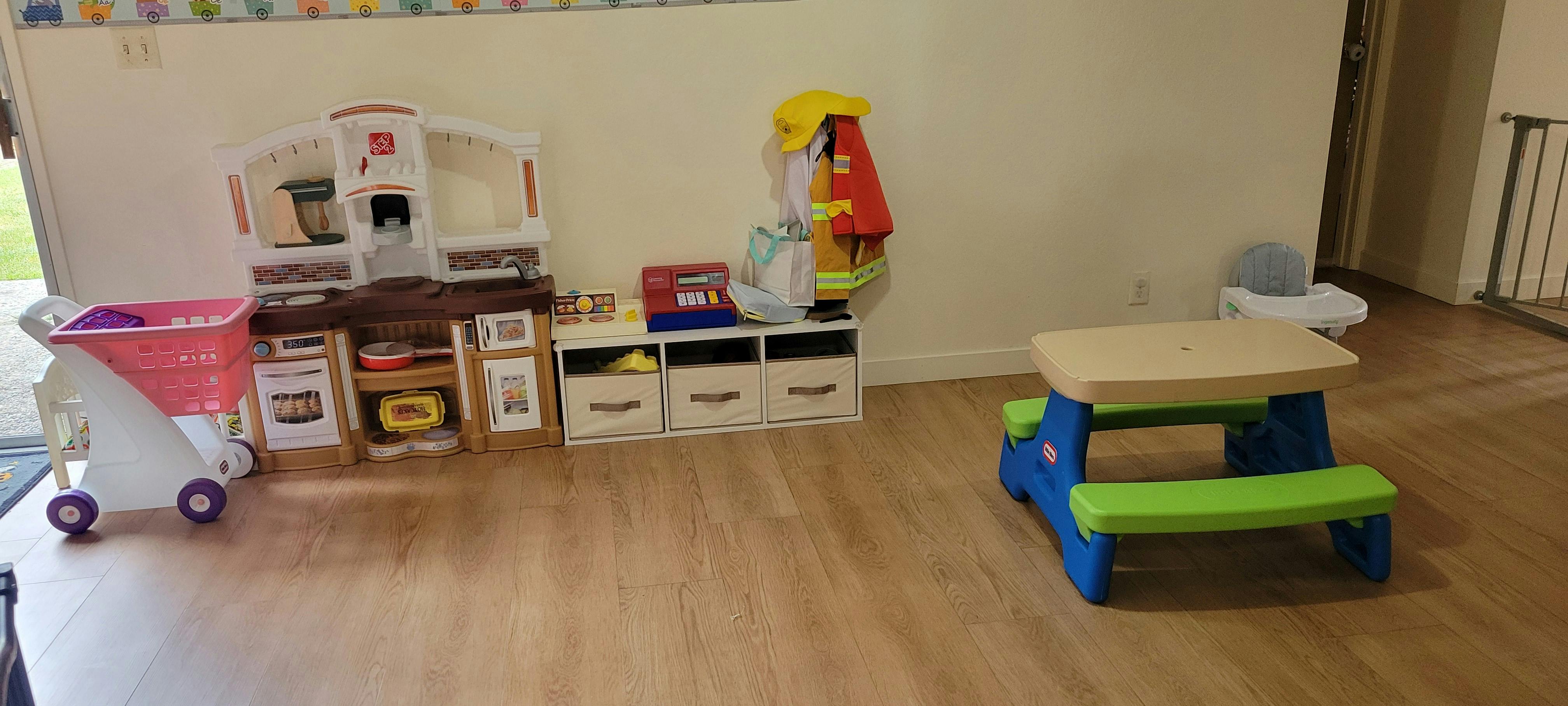 Play kitchen, grocery cart, and child-sized picnic table on a wood floor