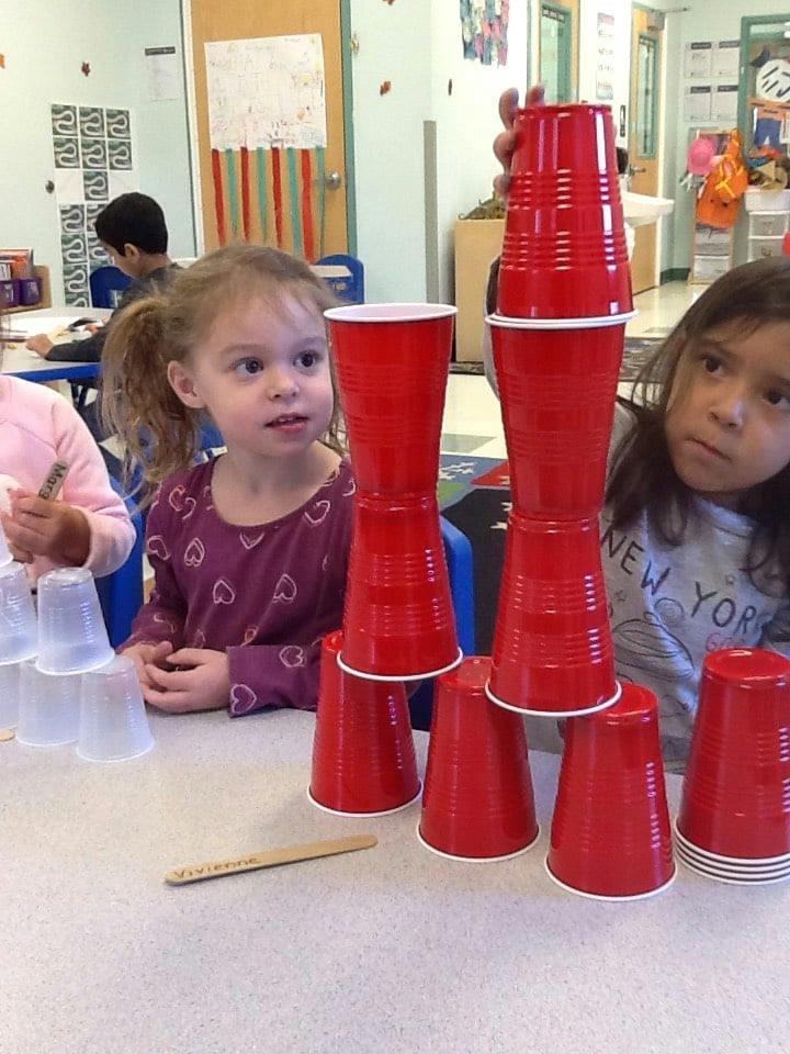 Two children building structures with red plastic cups in a classroom