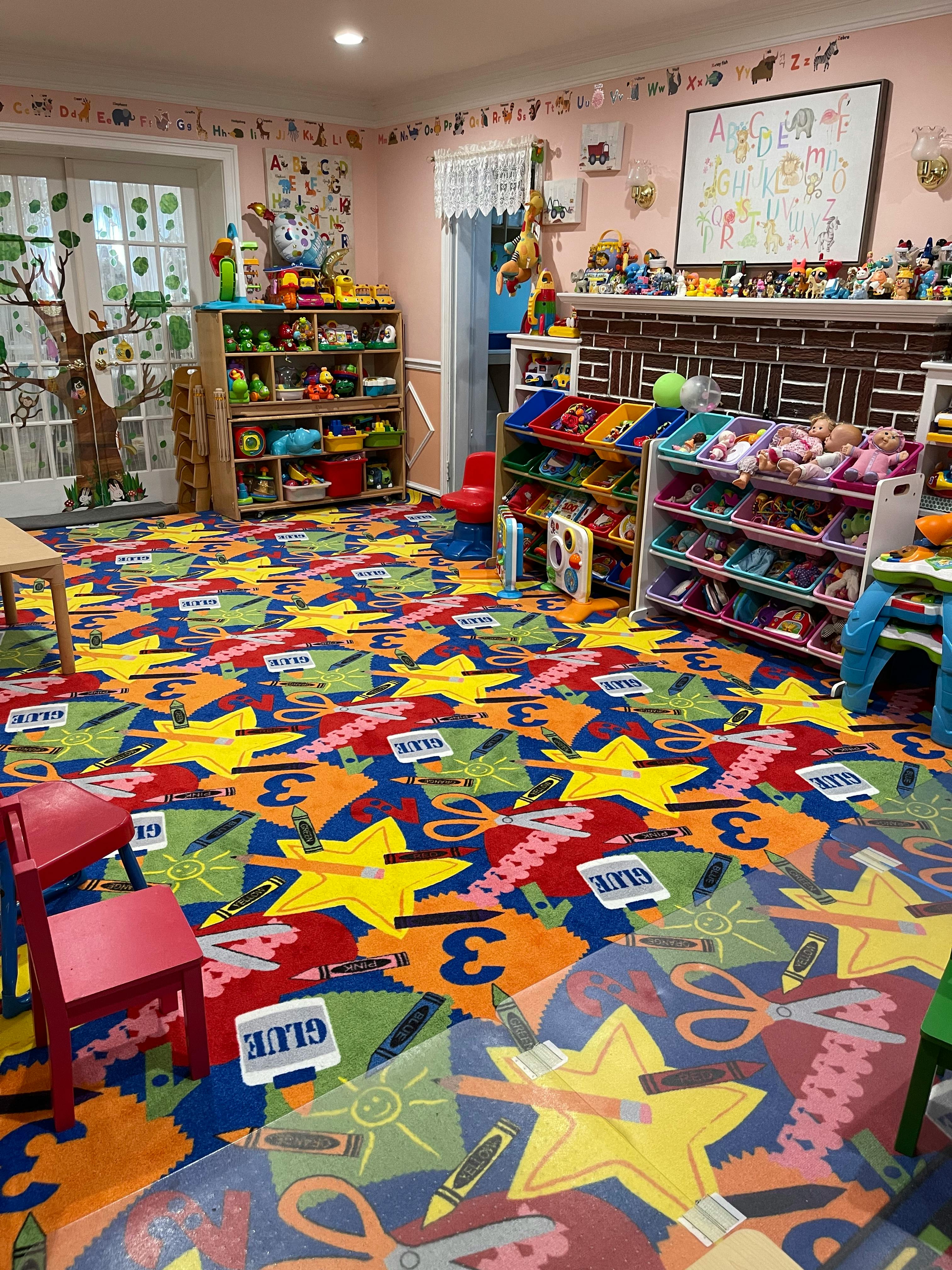 Playroom with colorful patterned carpet, shelves of toys, and small furniture