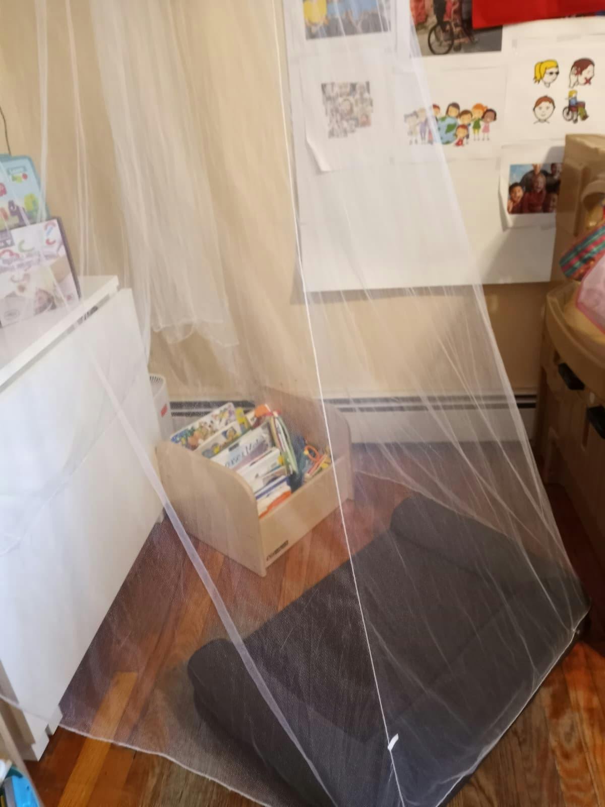 Reading nook with a mesh canopy covering a floor cushion and a book bin
