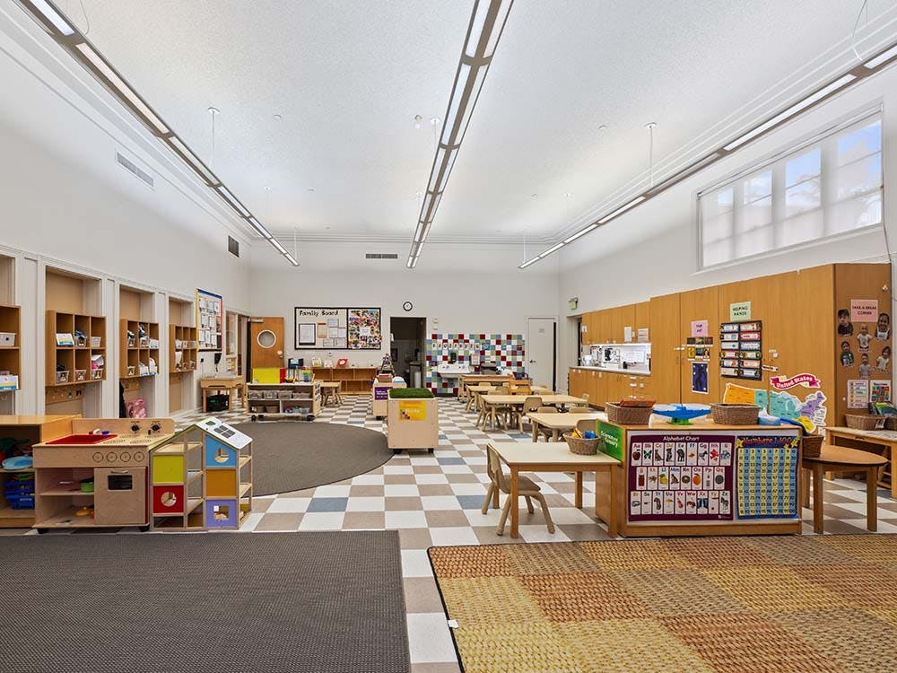 Empty preschool classroom with small tables, chairs, and play areas