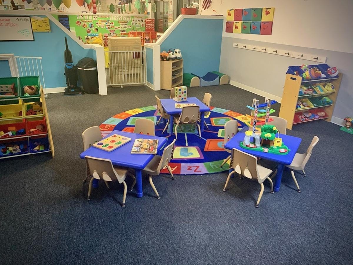 Classroom with small blue tables and chairs on a colorful rug