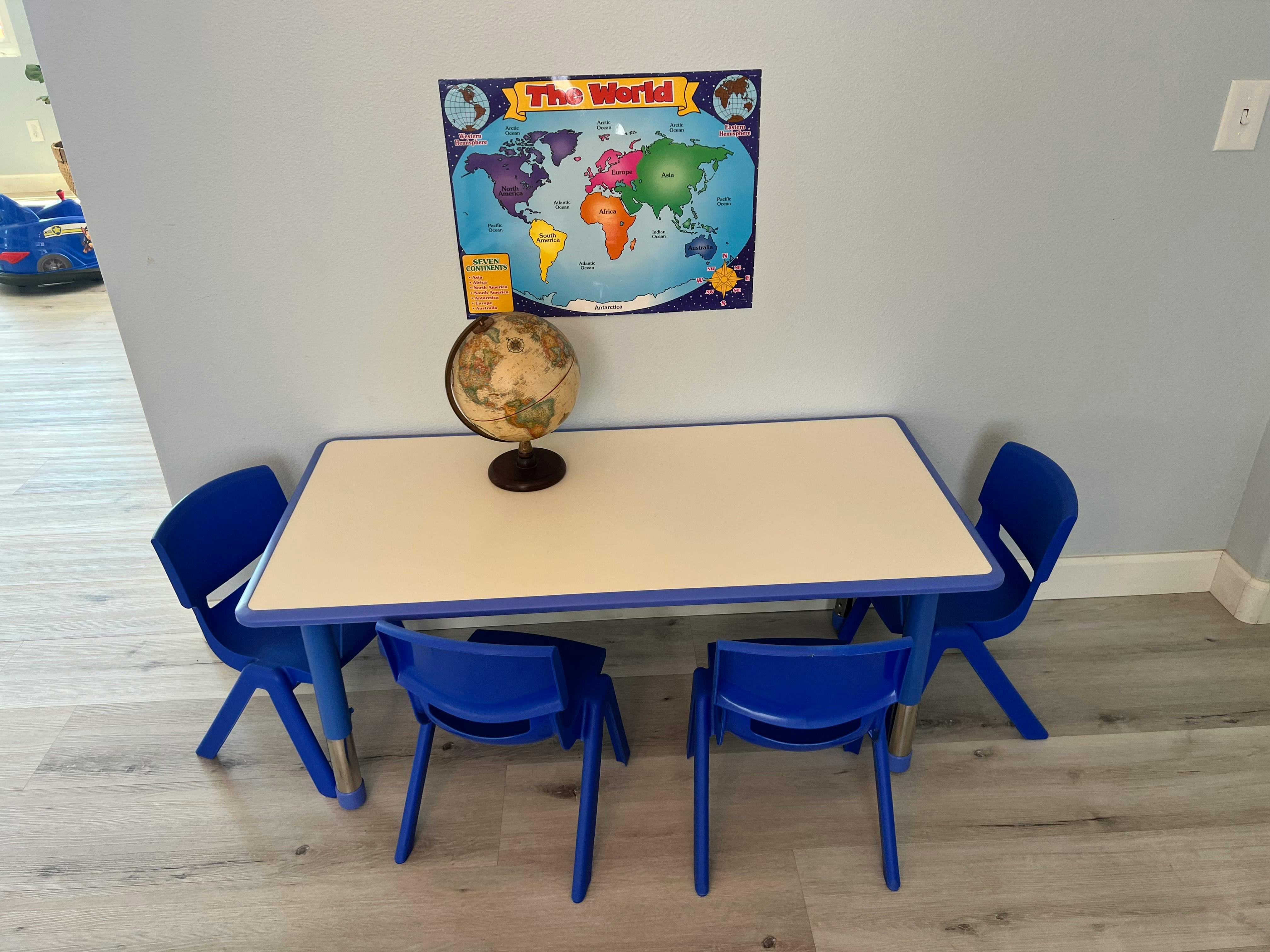 Table with four blue chairs, a globe, and a world map on the wall
