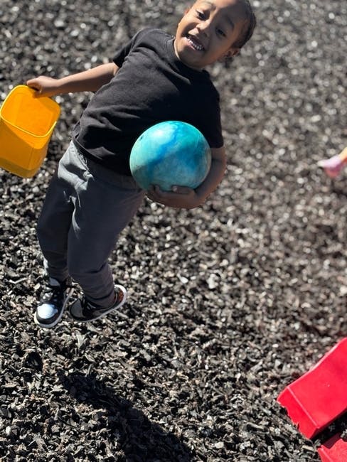 Child holding a blue ball and yellow bucket on a playground