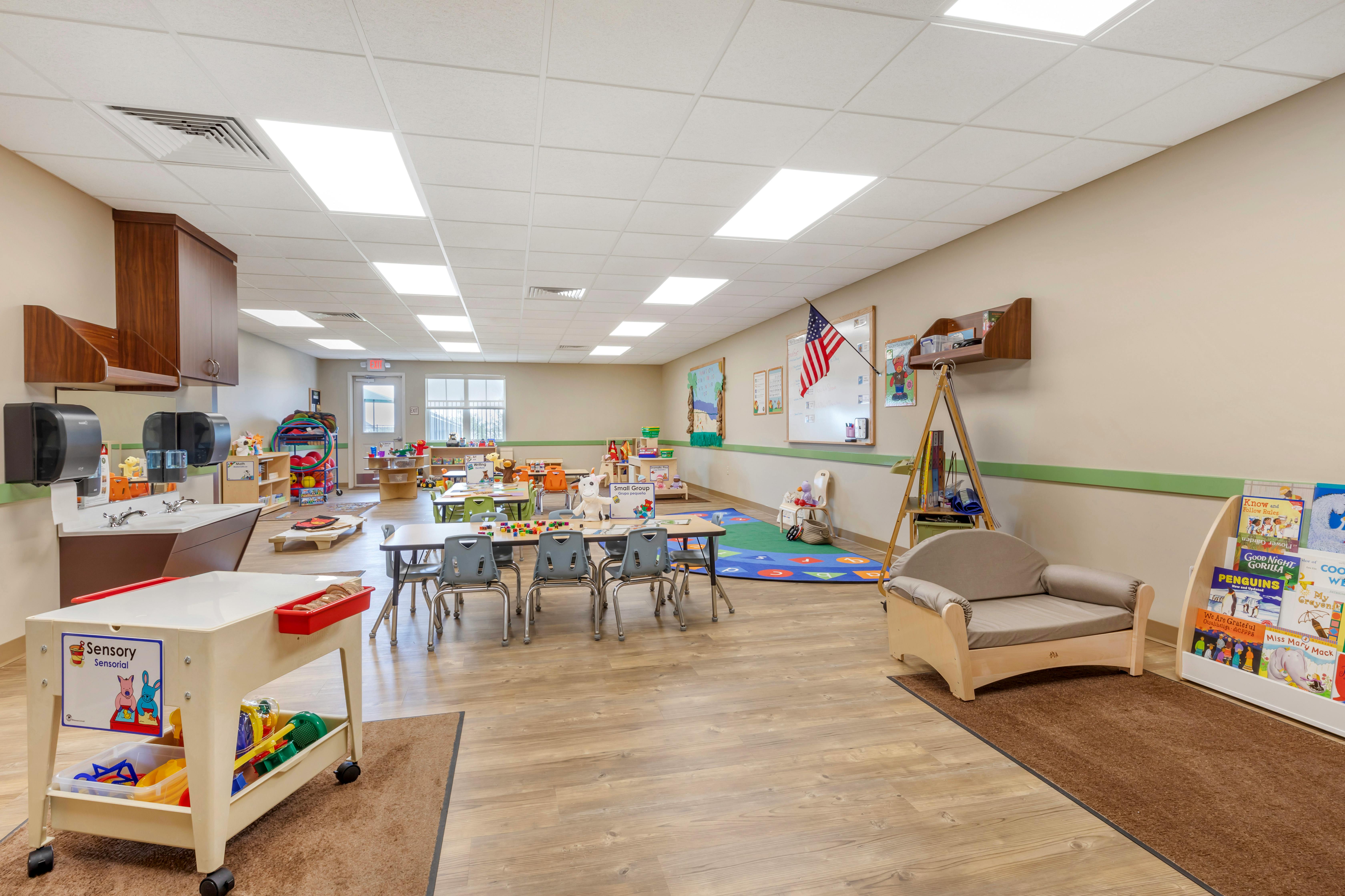 Classroom with children's tables and chairs, play areas, and a sink