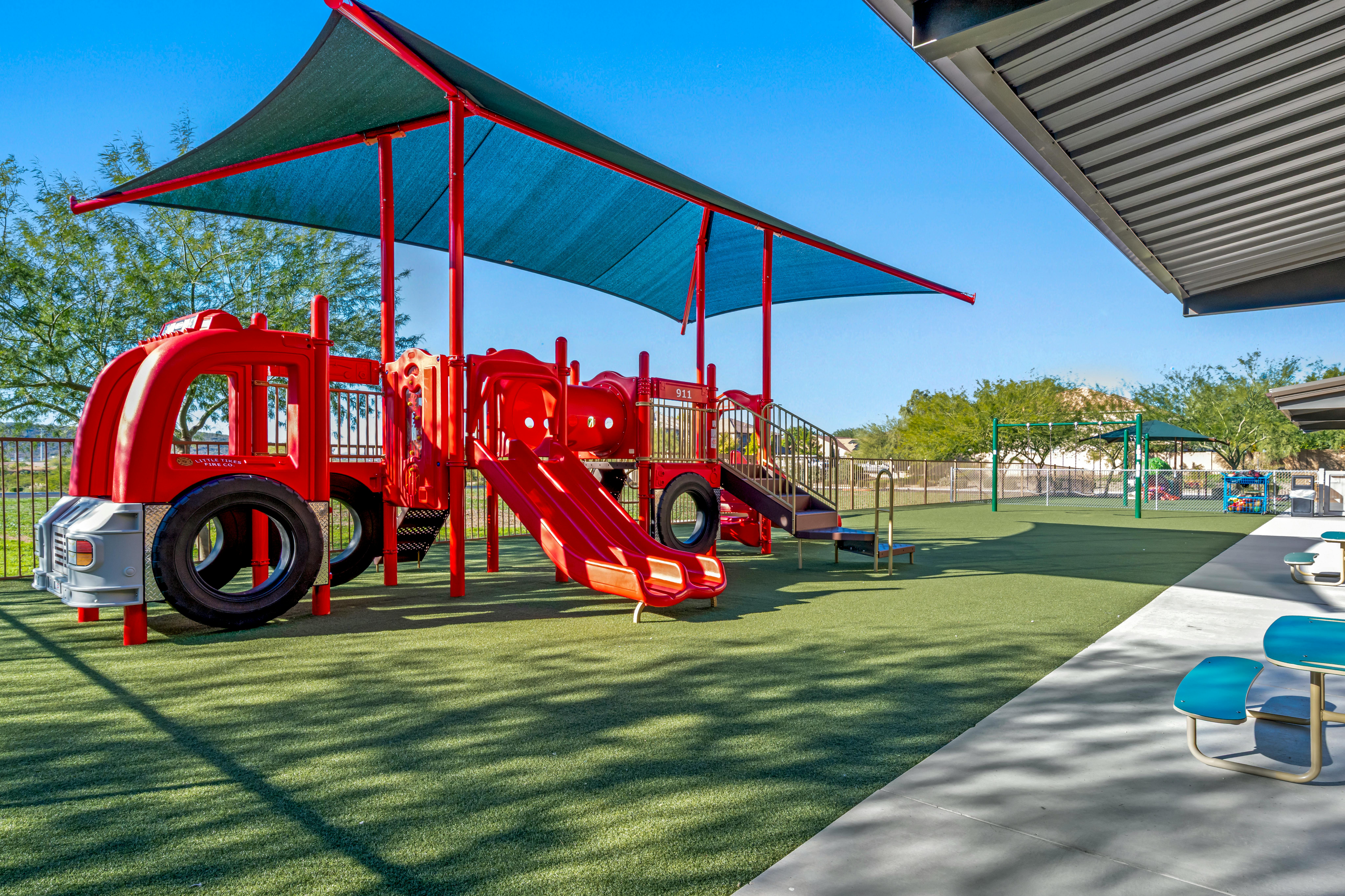 Red playground structure with slides under a blue shade covering on artificial grass