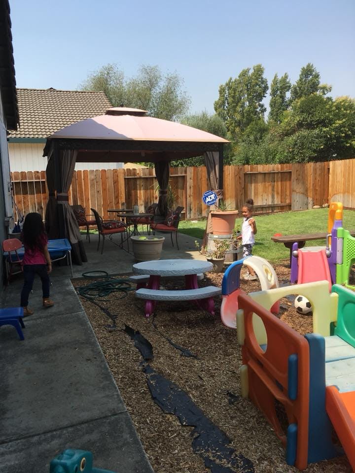 Two children in a backyard with a play area and a patio with a gazebo