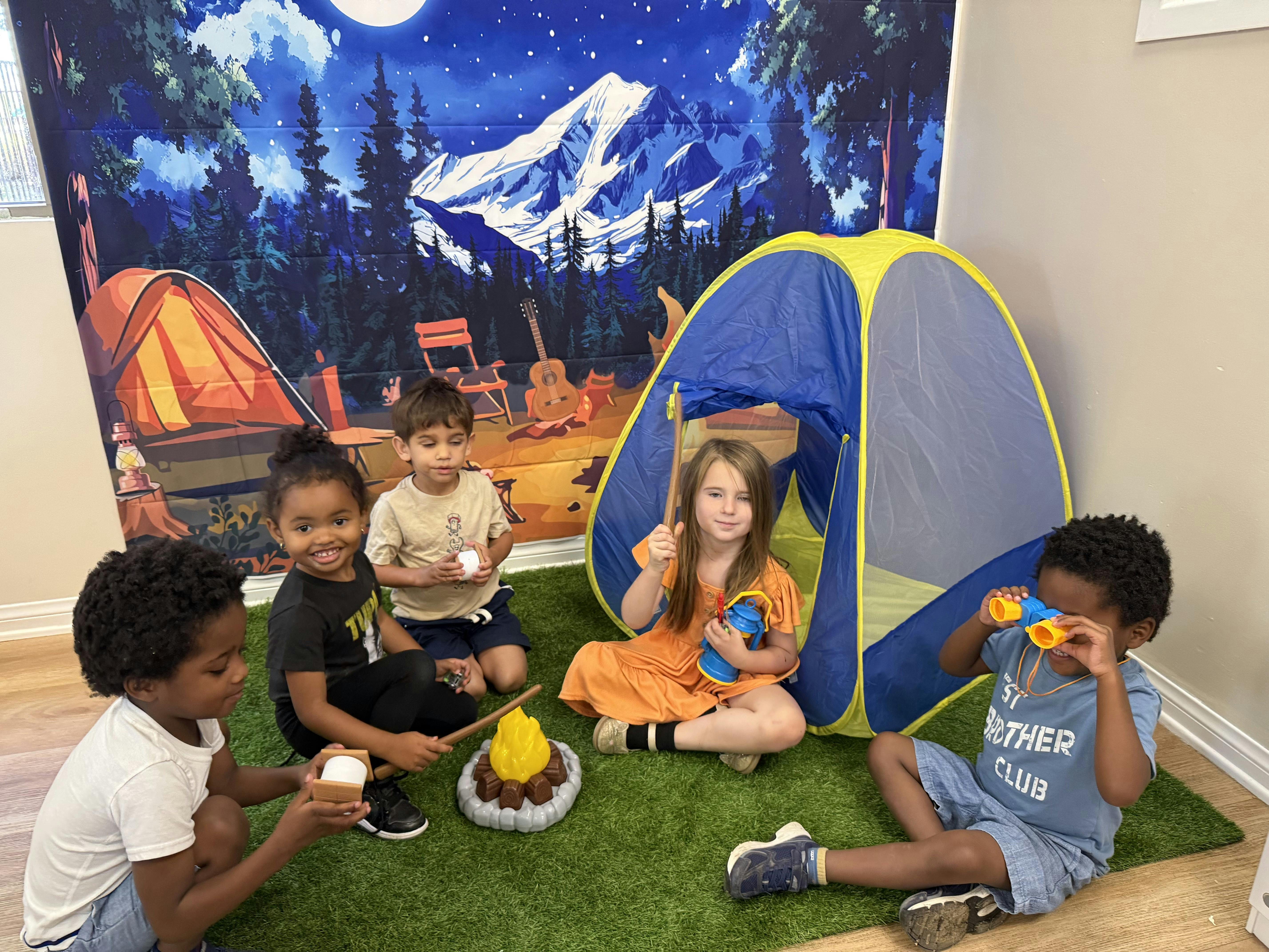 Four children playing with camping toys on an artificial grass mat