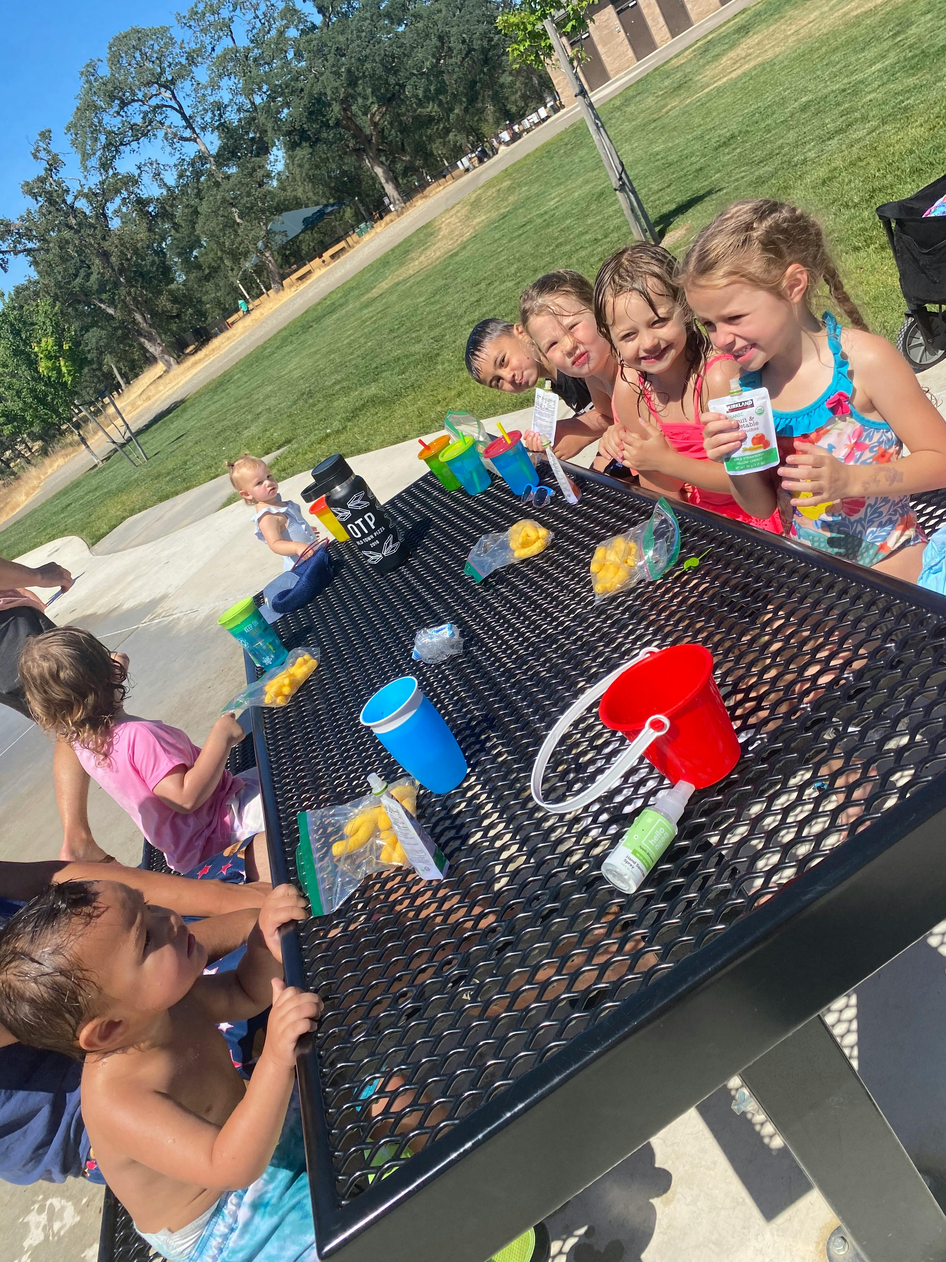 Children gathered around a picnic table with snacks and toys