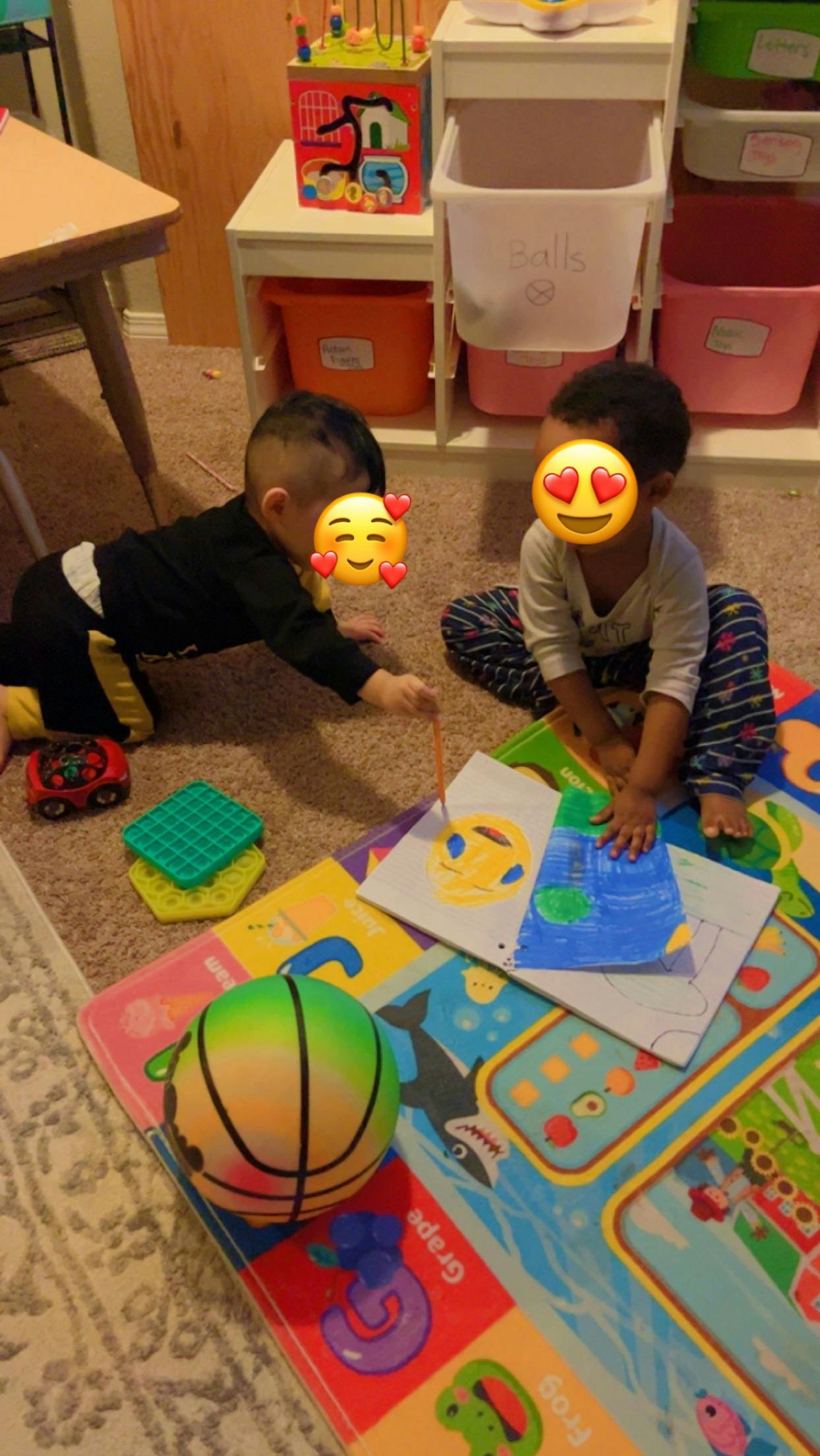 Two children playing on a mat with toys and drawings