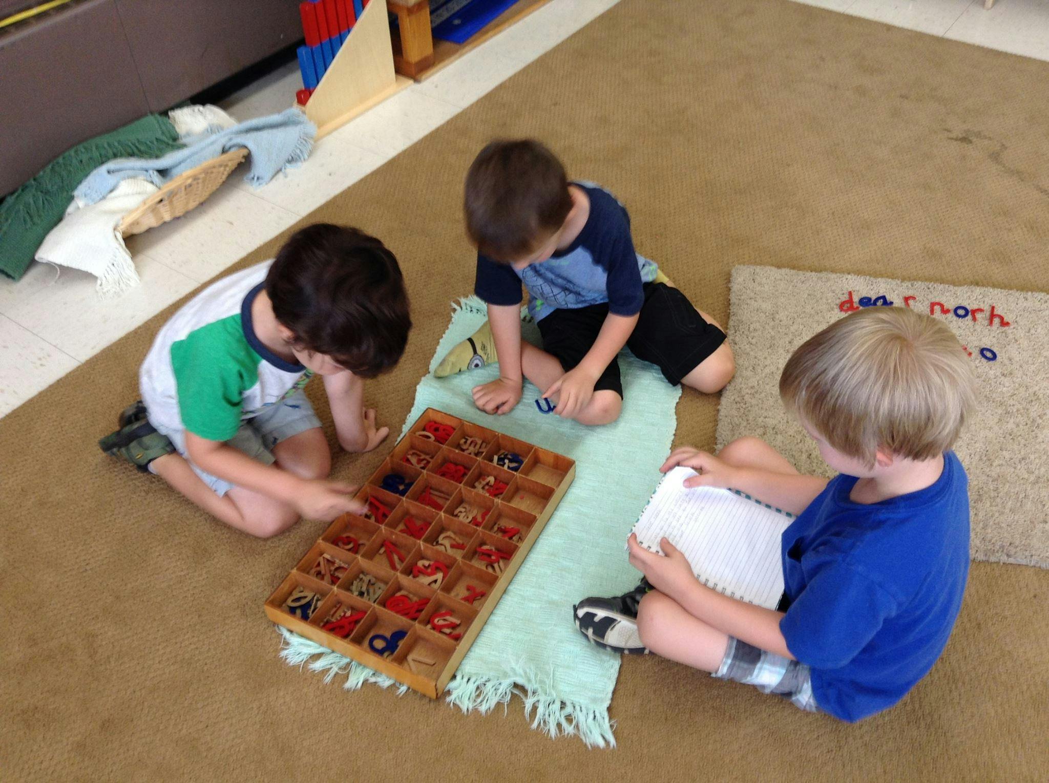 Three children on the floor playing with a wooden letter tray
