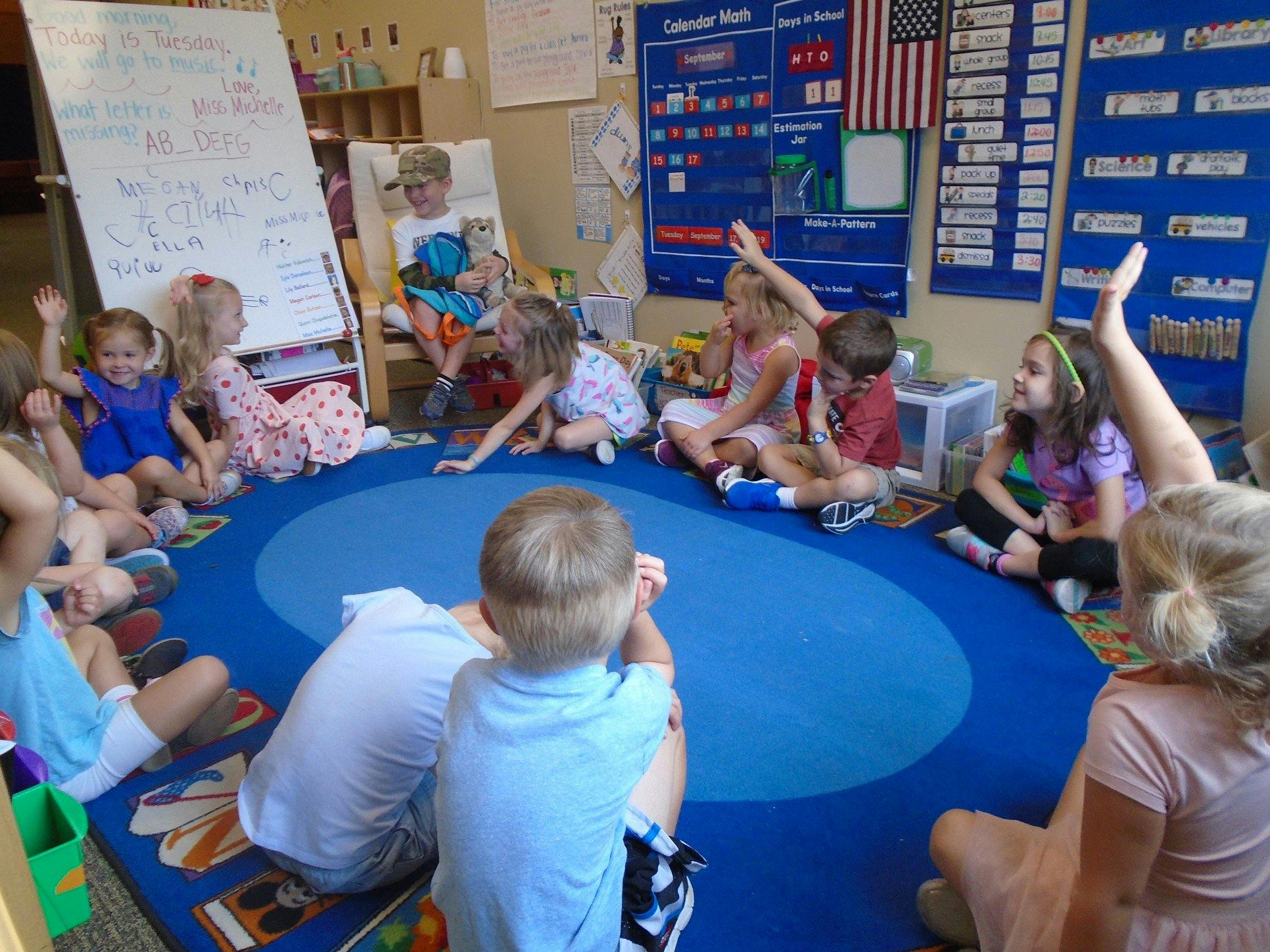 Children sitting in a circle on a blue rug in a classroom