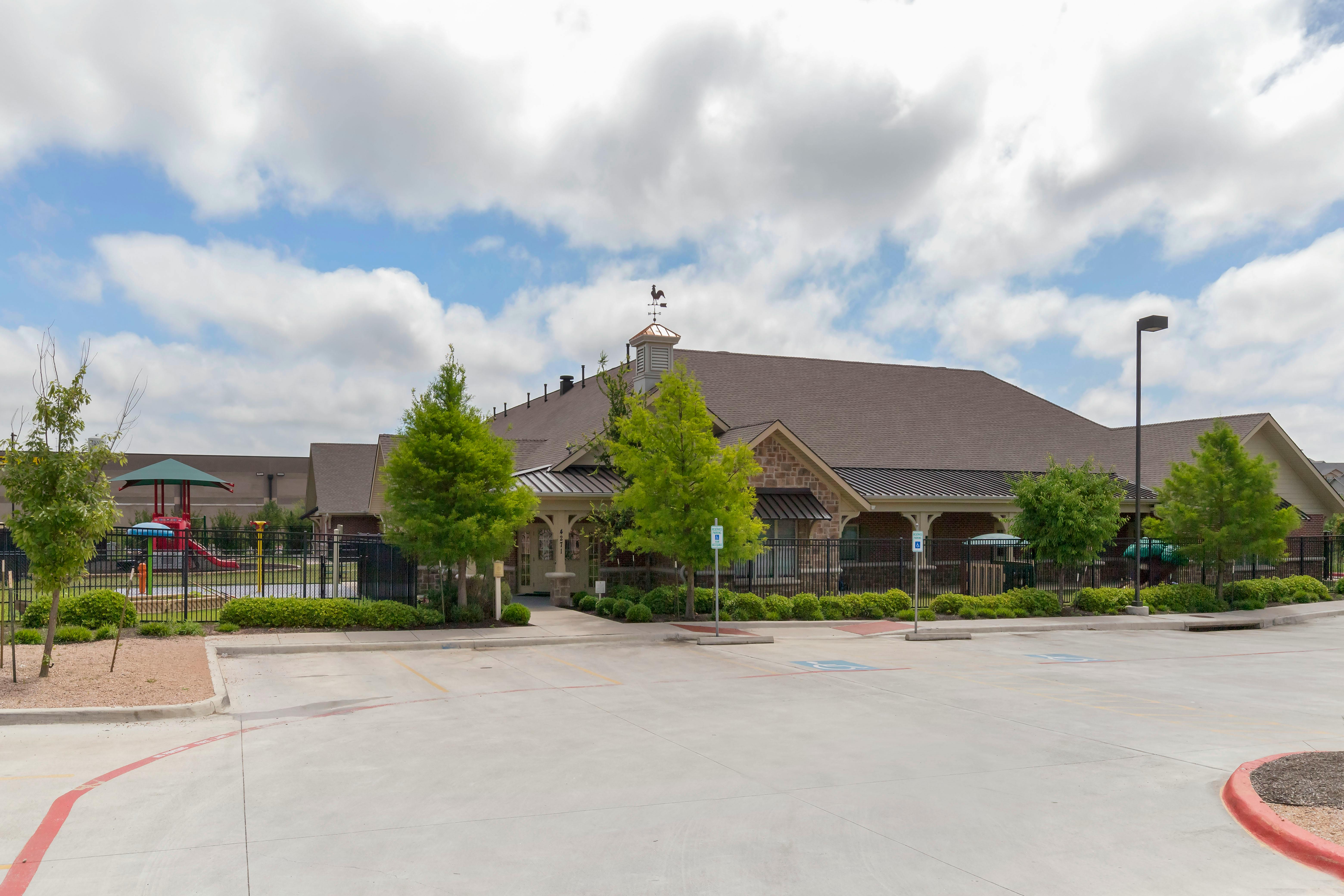 A low-rise building with a weathervane on the roof, parking lot in front