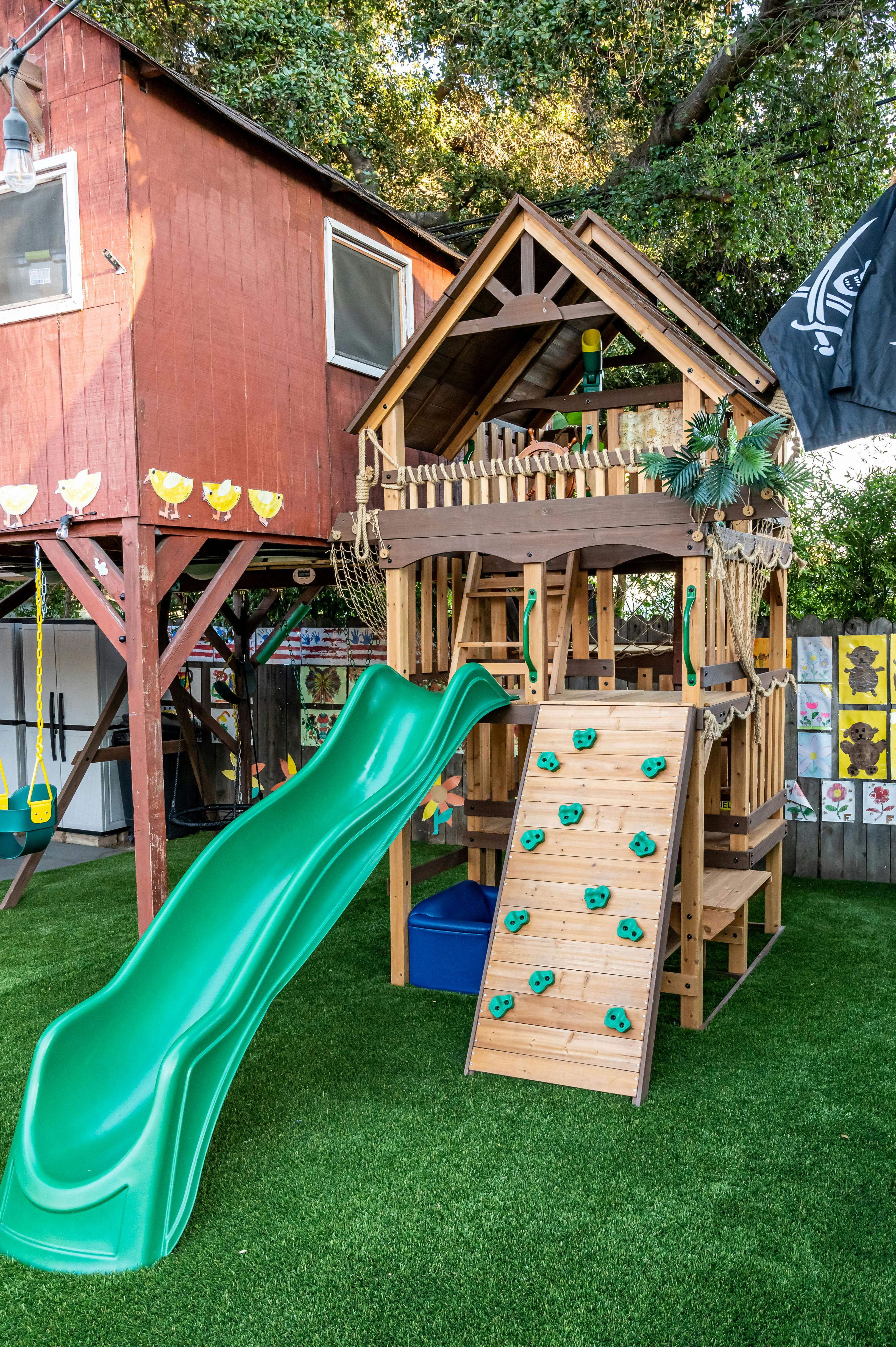 Wooden playset with a green slide and climbing wall in a backyard