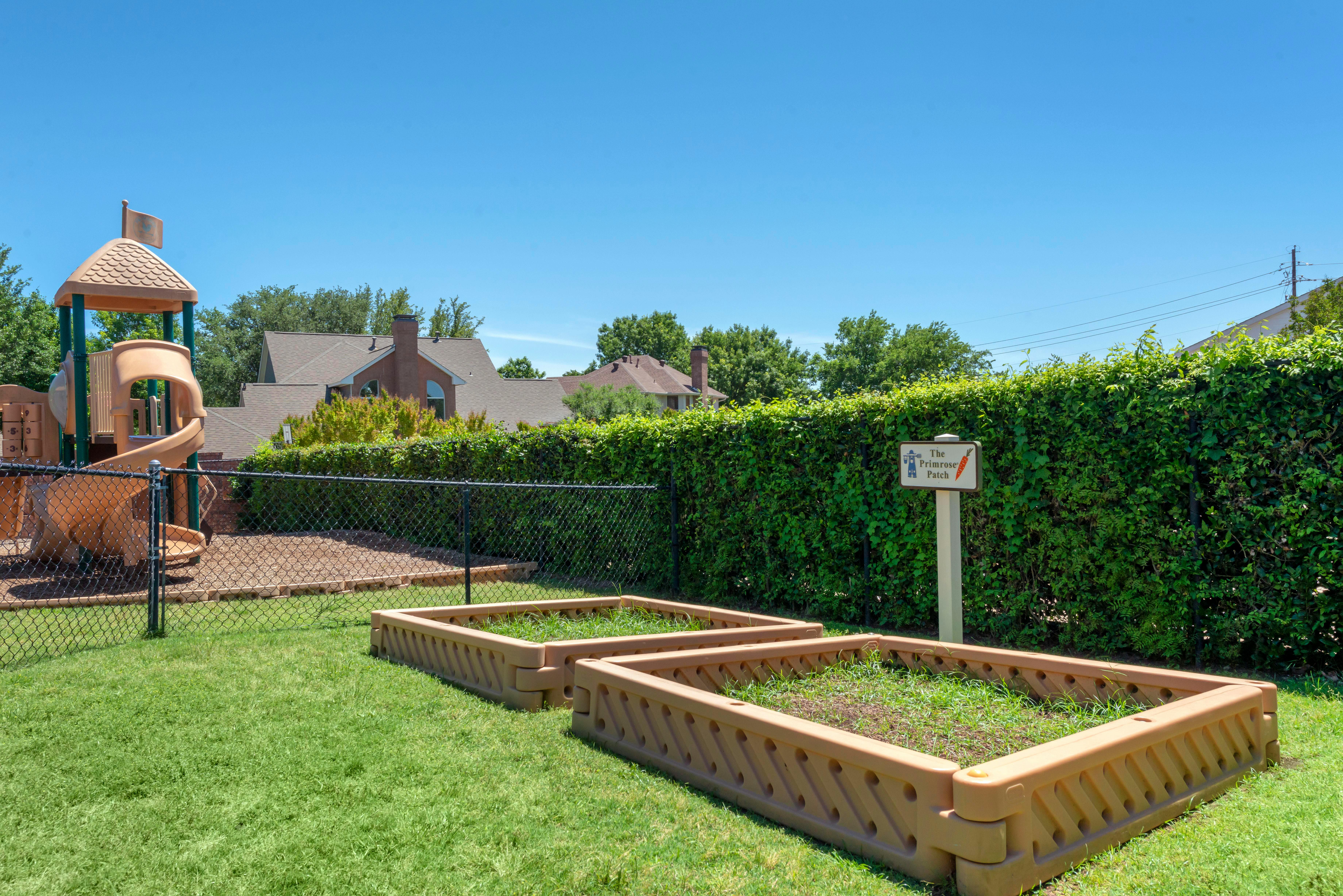 Playground with raised garden beds and a sign for "The Primrose Patch"