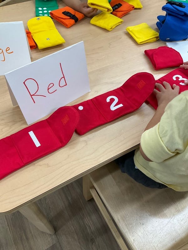 Child manipulating red fabric number strips on a table with color signs