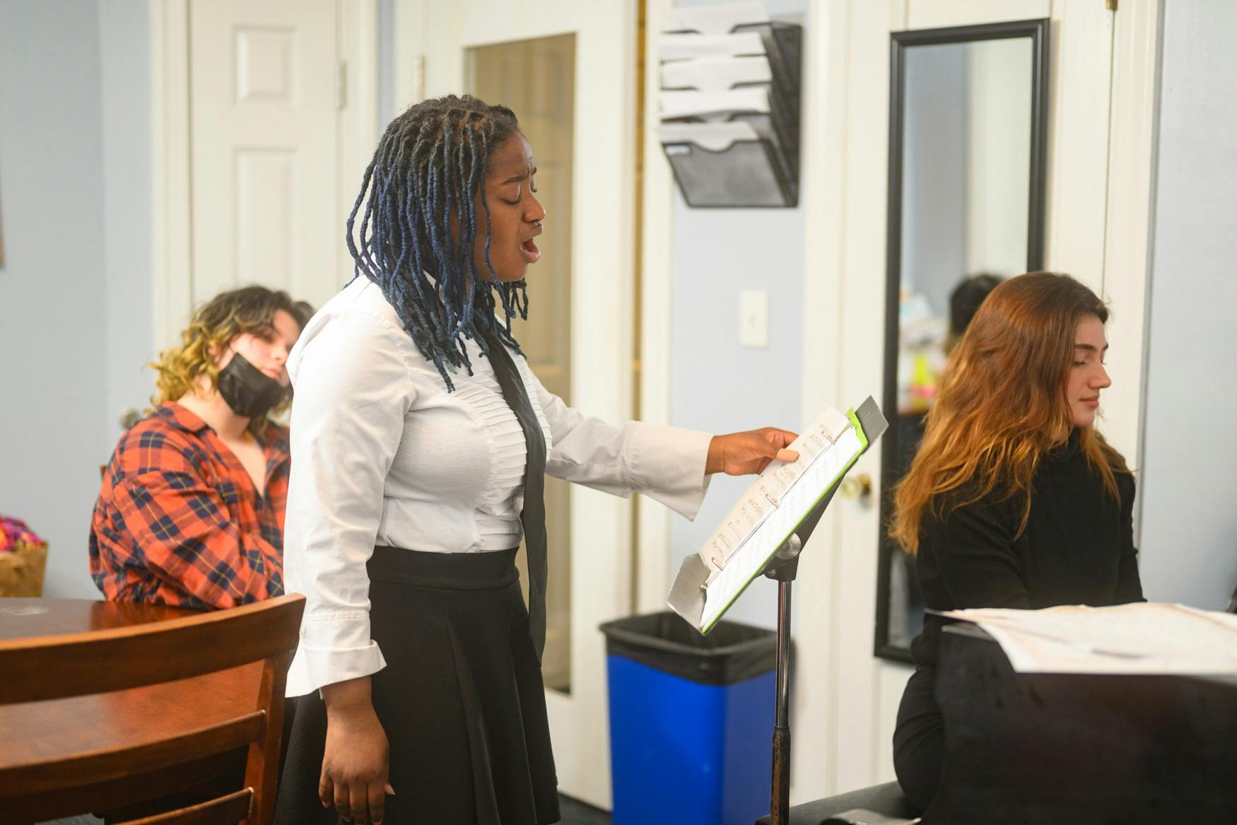Person speaking while pointing at a music stand with other people in the background