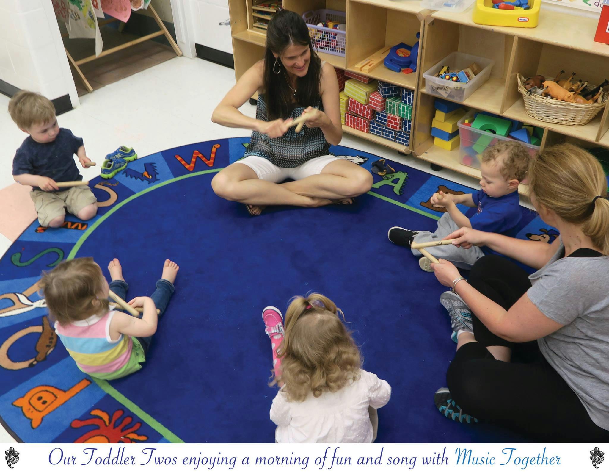 Adults and children sitting on a rug playing with rhythm sticks