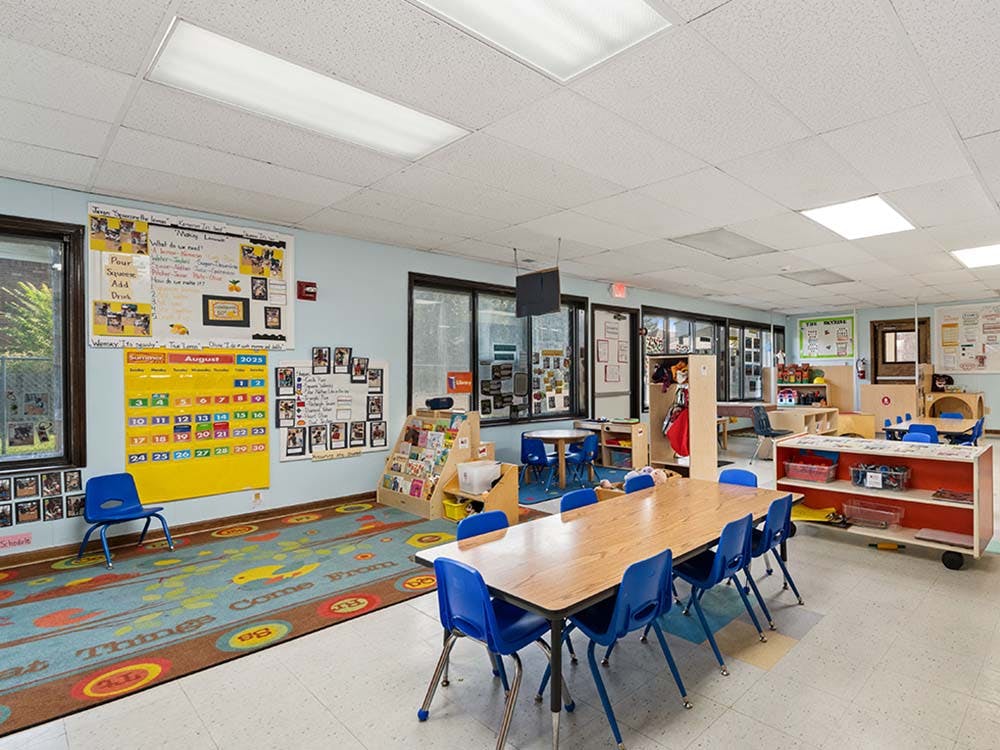 An empty classroom with small tables and blue chairs