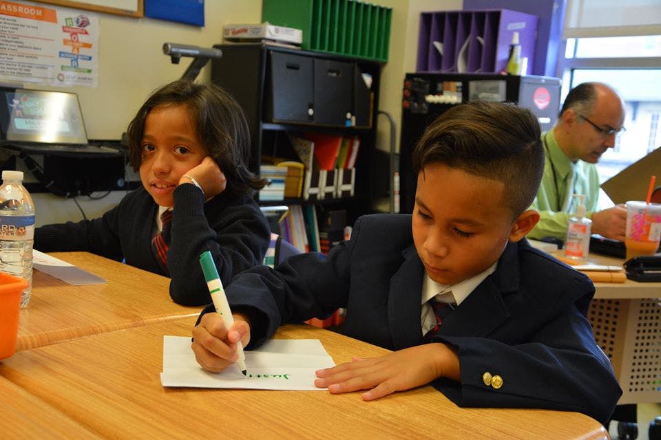 Two children in uniform writing at desks in a classroom