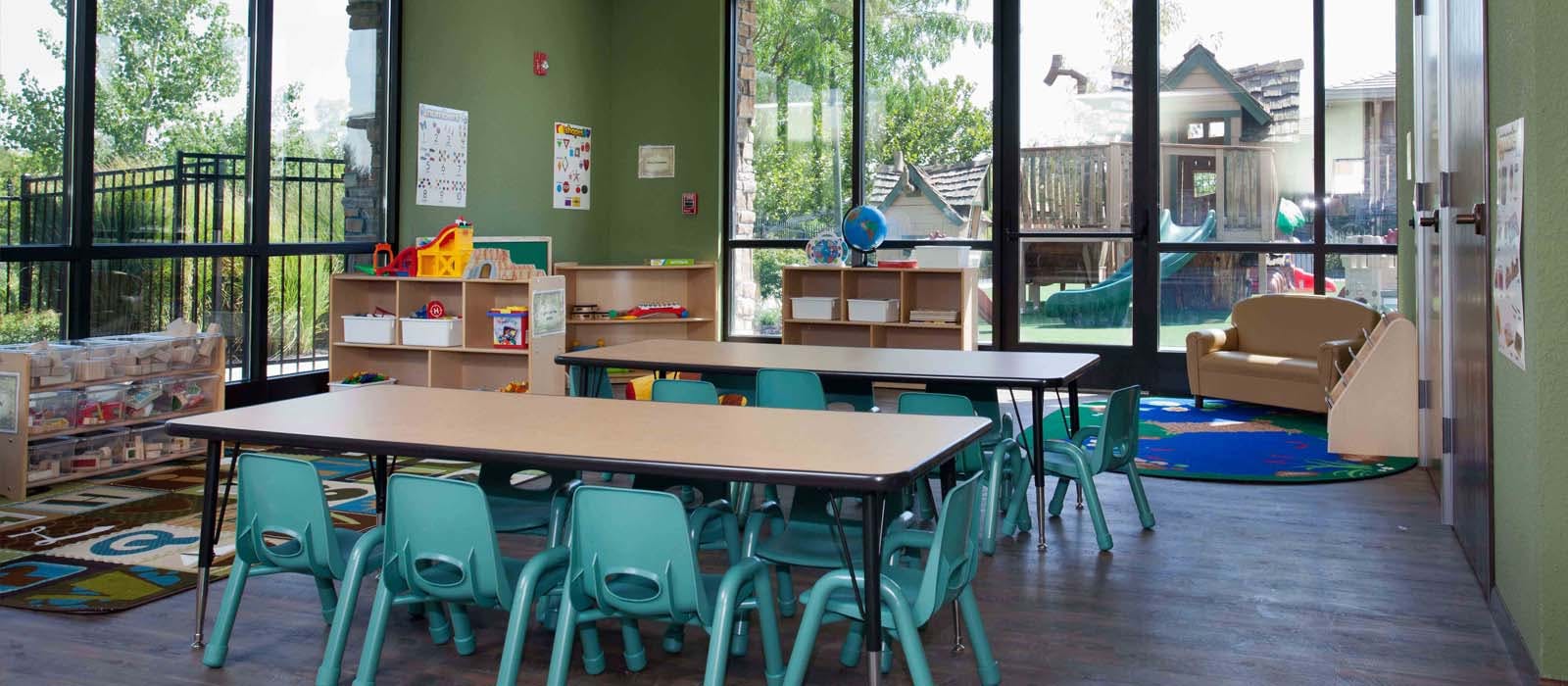 Classroom with tables and chairs, large windows overlooking an outdoor play area