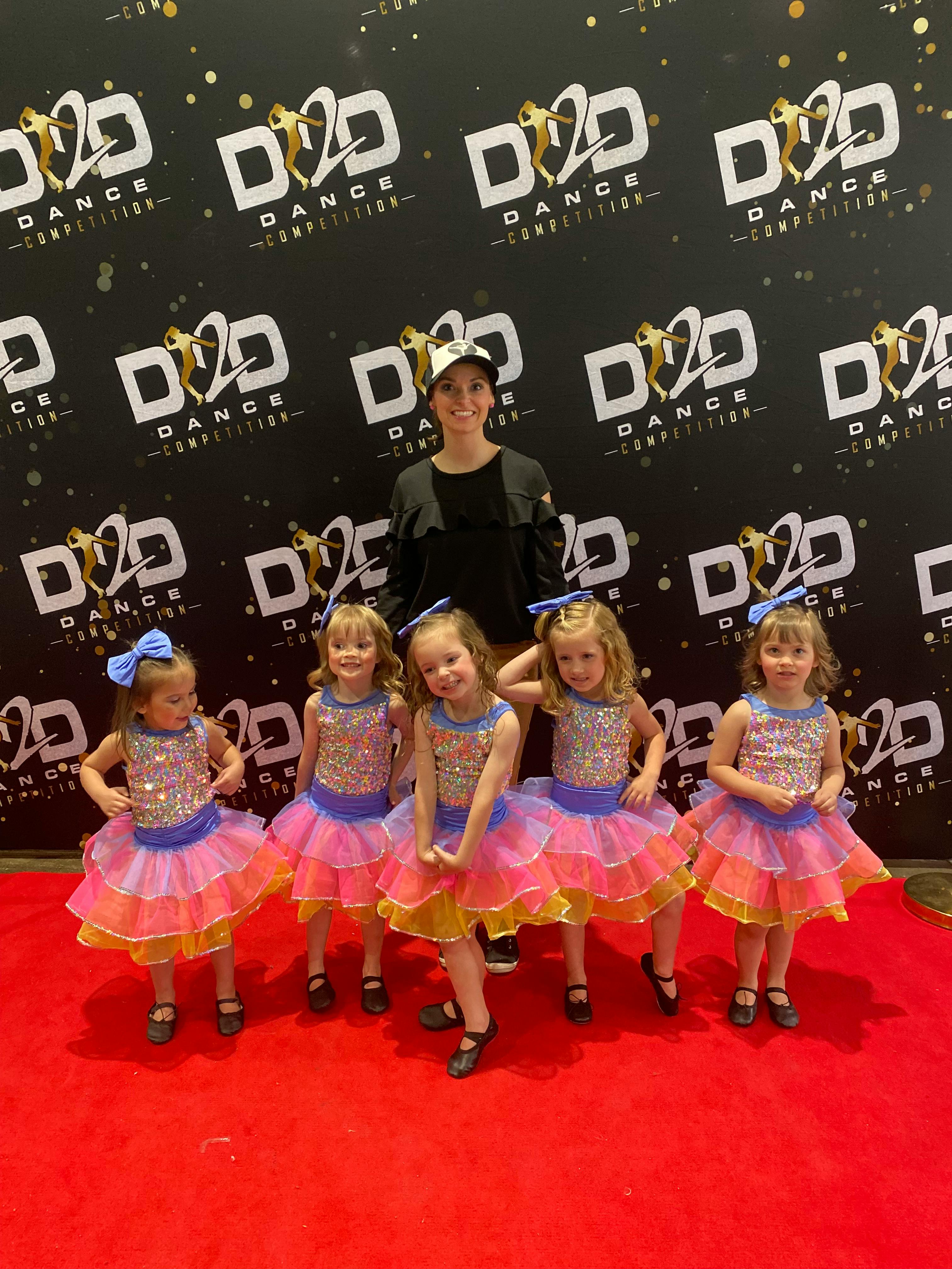 Person and four children in dance costumes posing on a red carpet