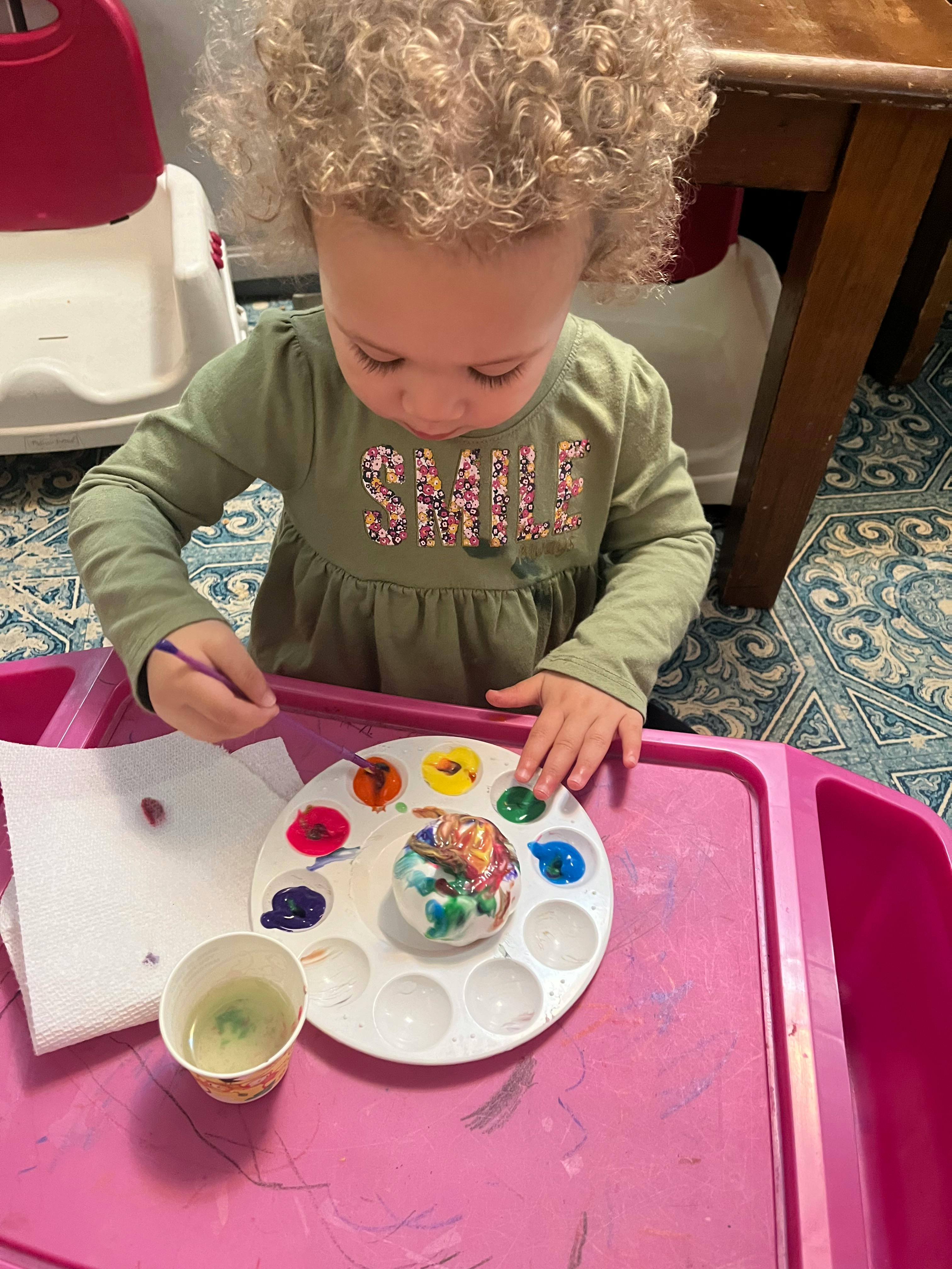 Child painting a small object with a paintbrush and paint palette
