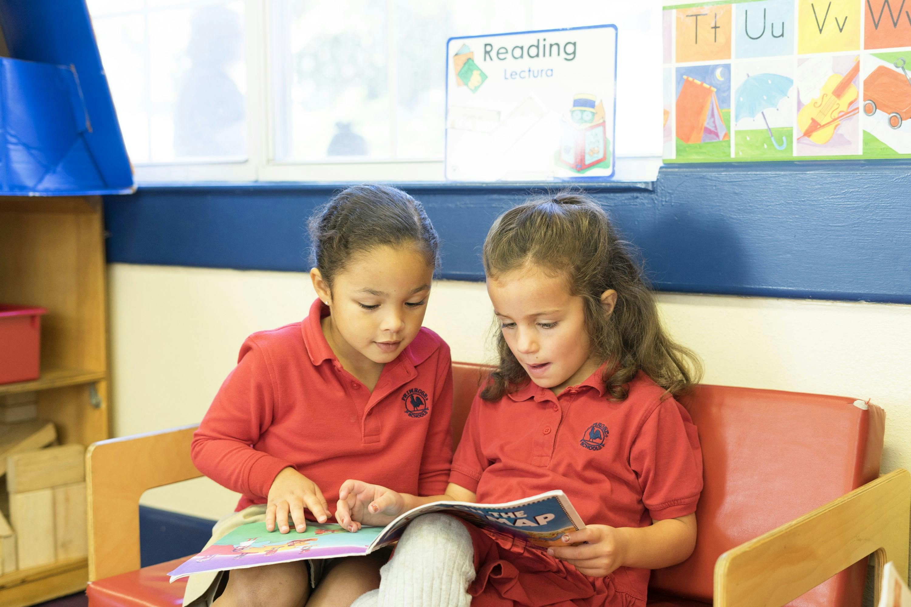 Two children in red shirts reading a book together in a classroom
